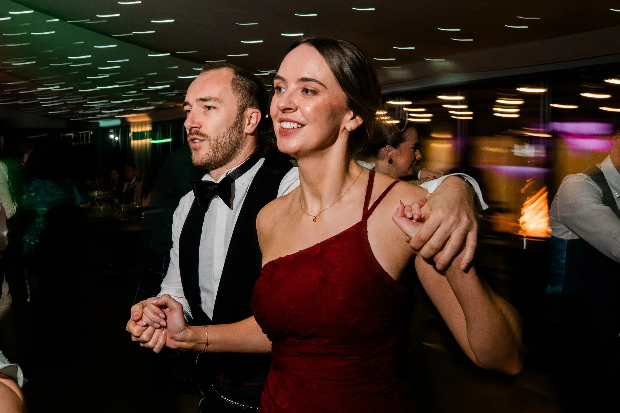 Two wedding guests dance arm in arm at the evening reception.