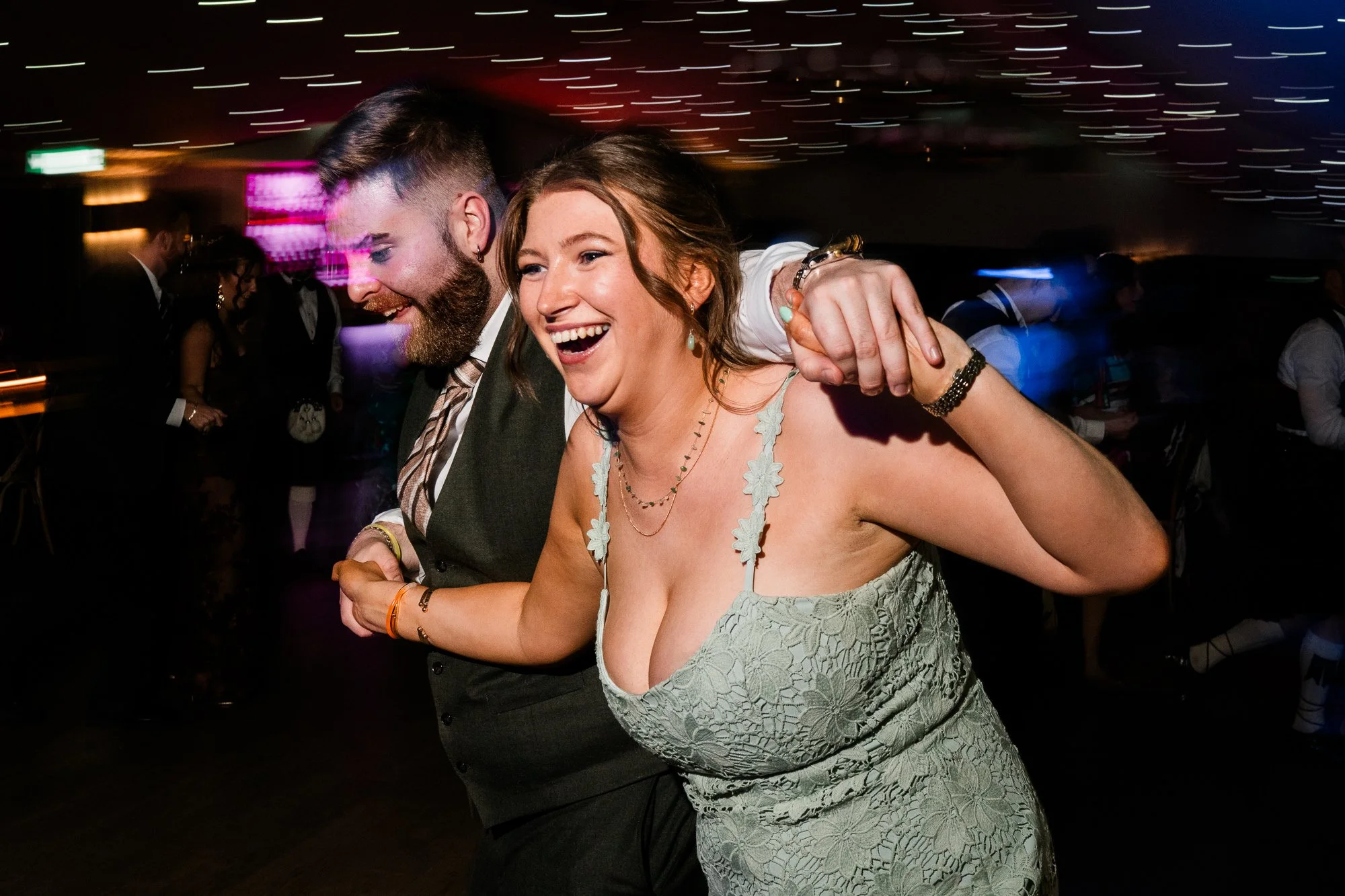 A bridesmaid in a pale green dress laughs on the dance floor.