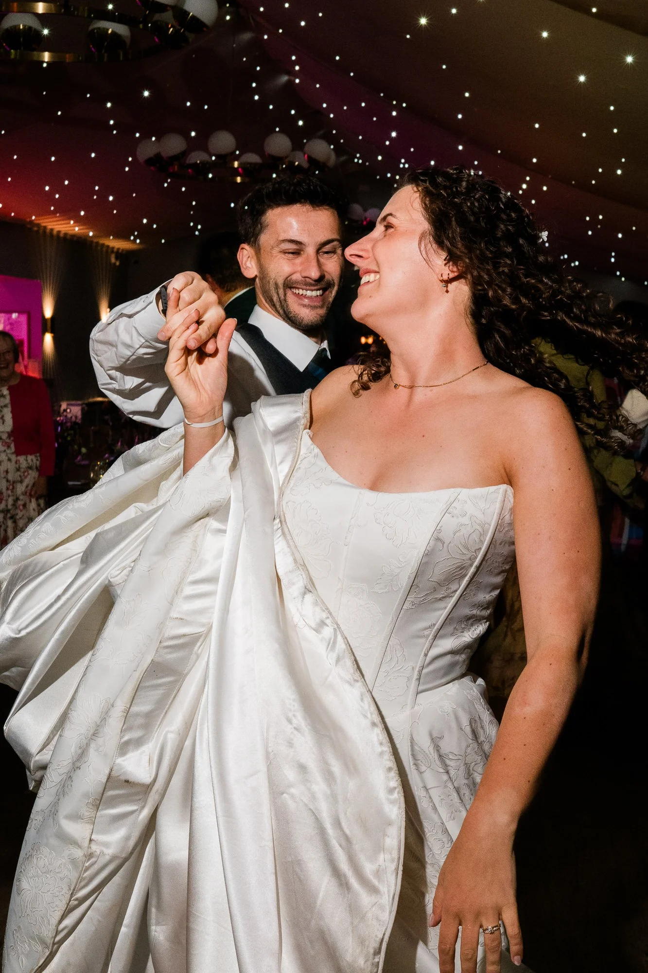 Aimee and Matthew laugh together on the dance floor, surrounded by their guests.