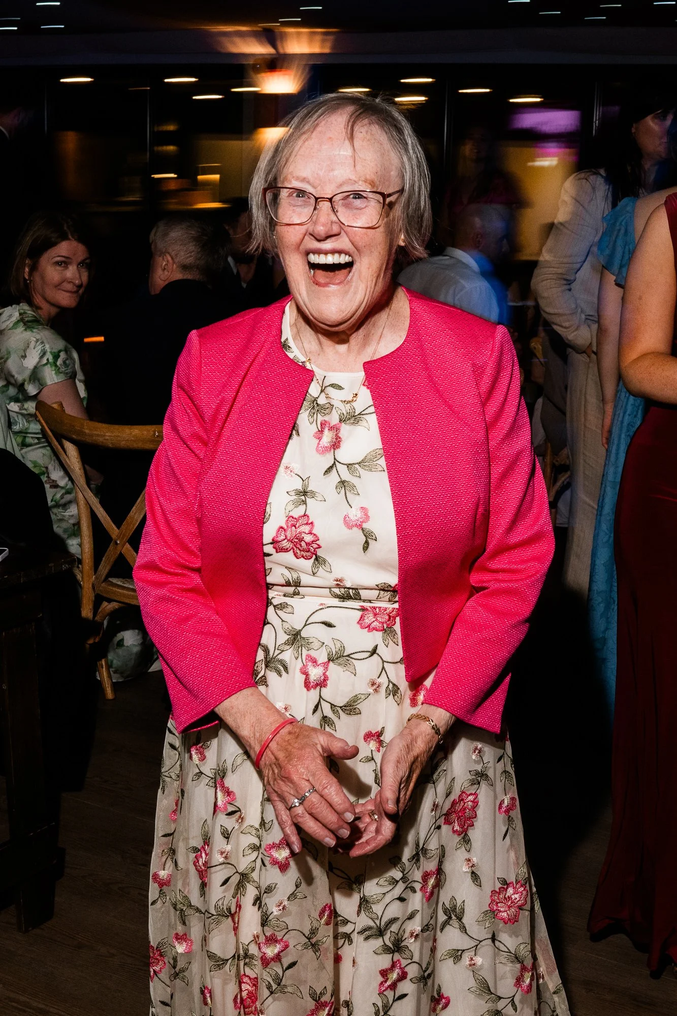 A wedding guest in a bright pink jacket laughs during the evening celebration.