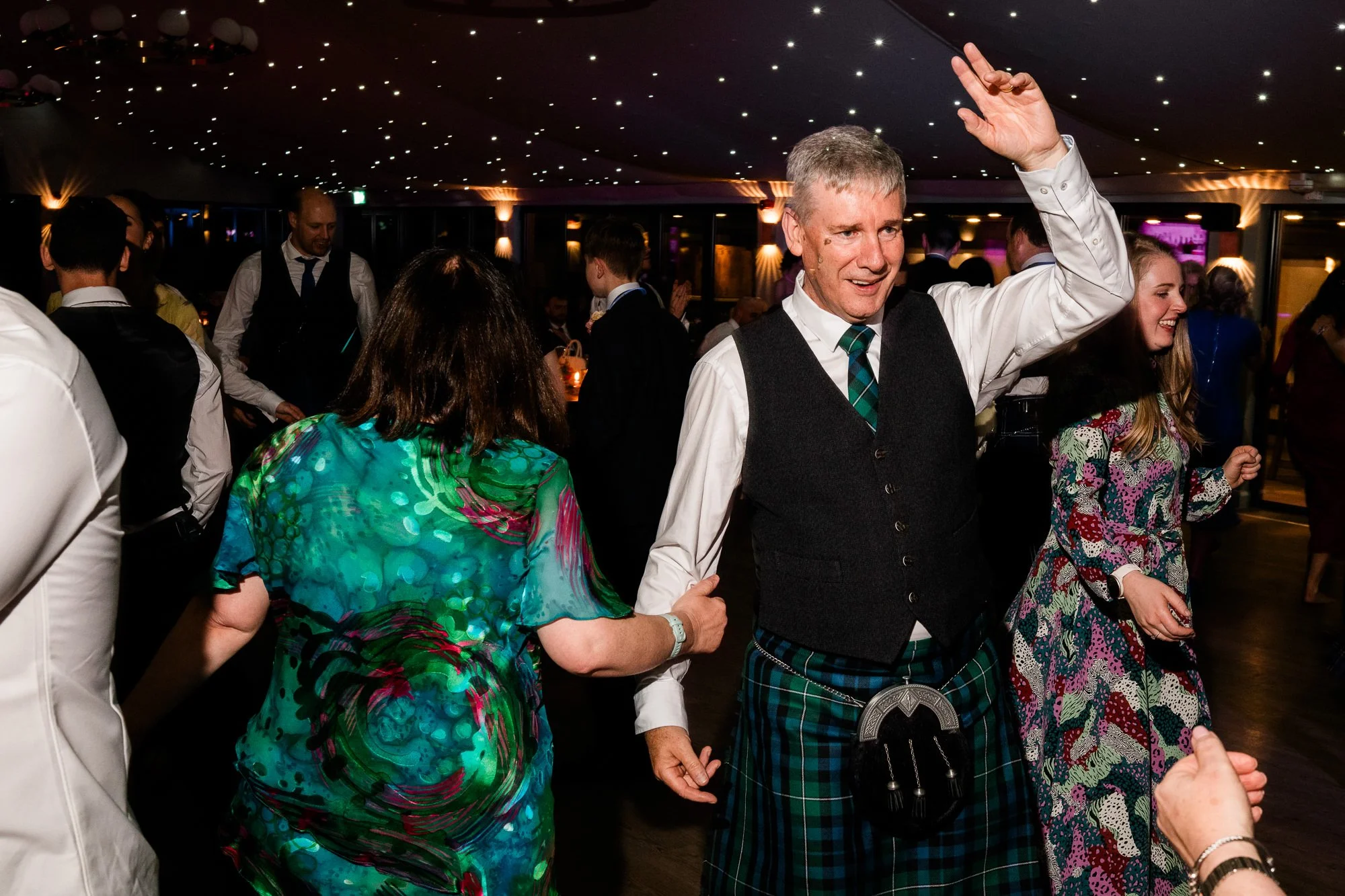 A wedding guest raises an arm while dancing at the reception.