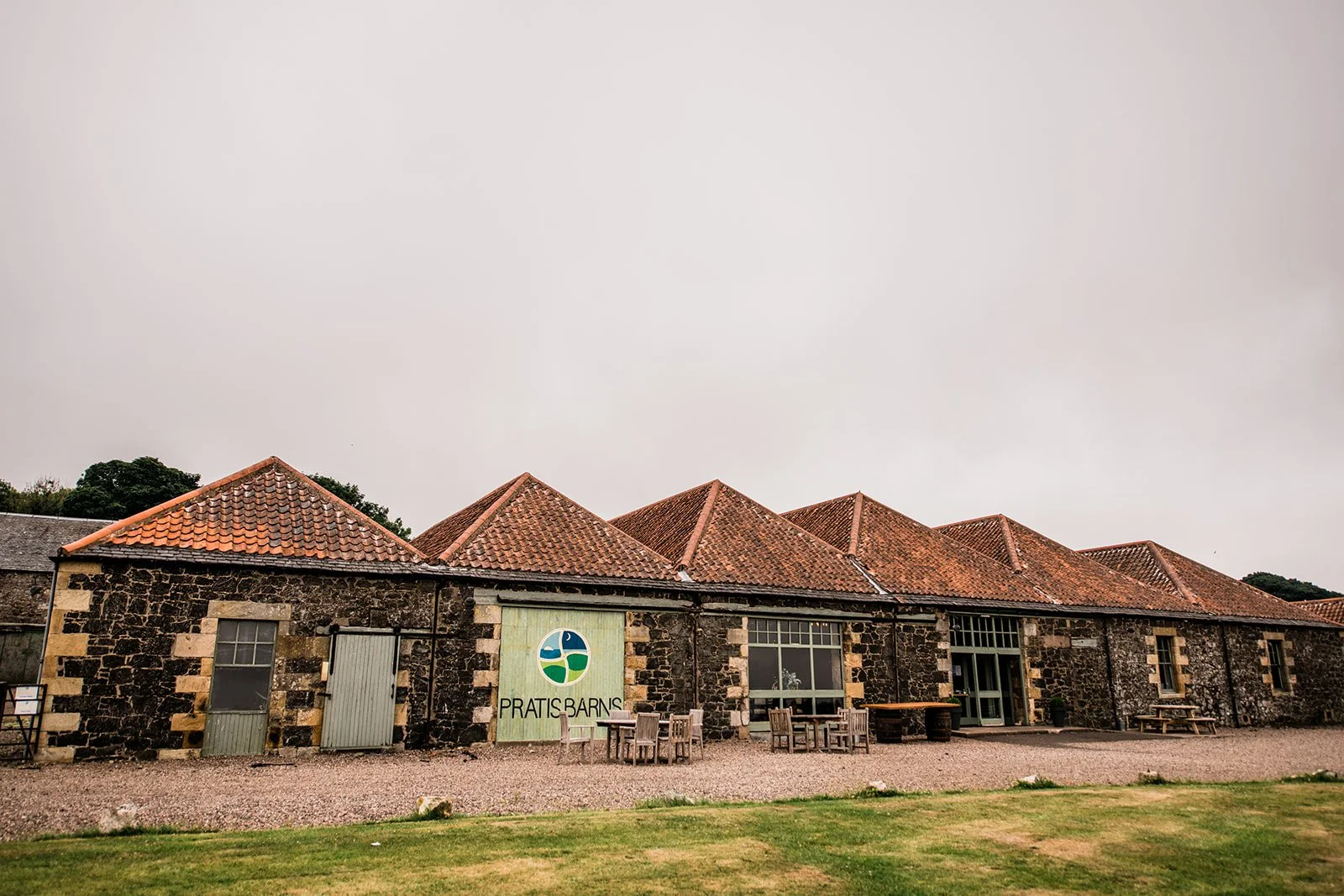 The stone barns and red tiled roofs of Pratis Barns beneath a cloudy Fife sky.