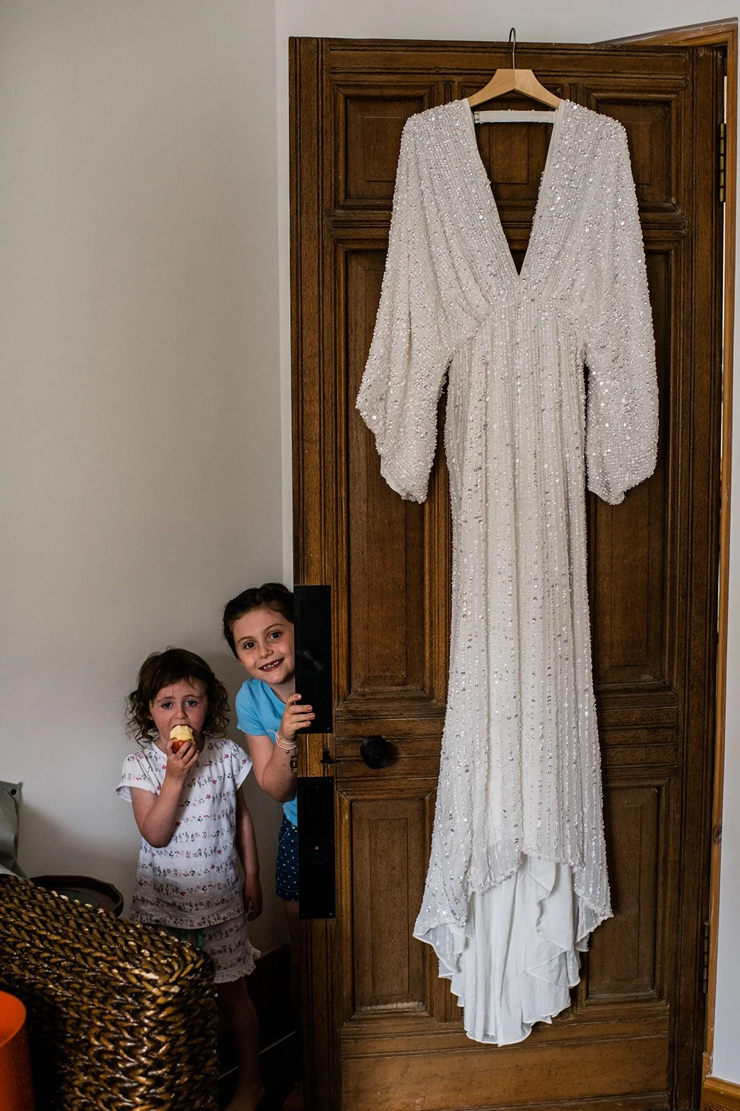 A beaded wedding dress hangs beside photographs in a doorway.