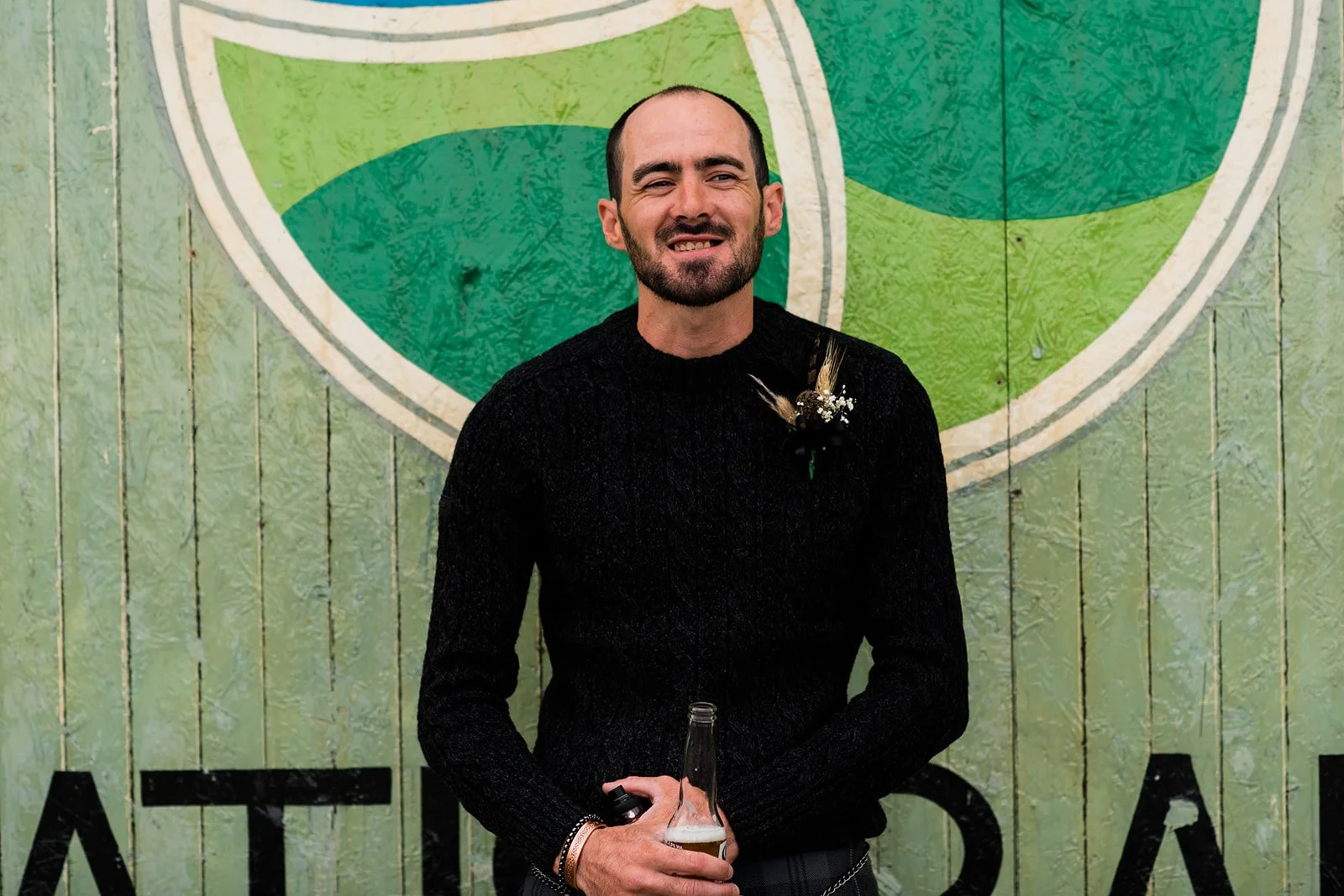 The groom smiles in front of a green painted door at Pratis Barns.