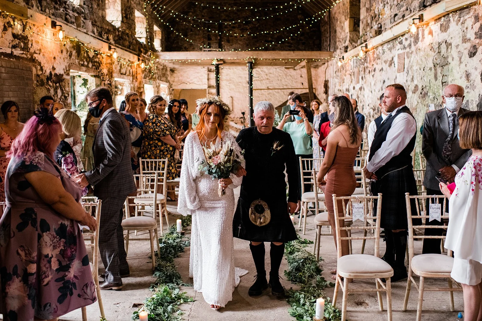 The bride enters the ceremony barn arm in arm with her escort.