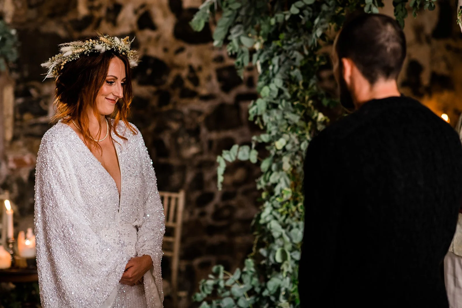 The bride smiles at the groom during their wedding ceremony beside the stone wall.