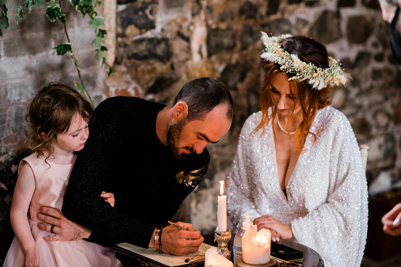The couple lean over the candle arrangement with a young flower girl during their ceremony.