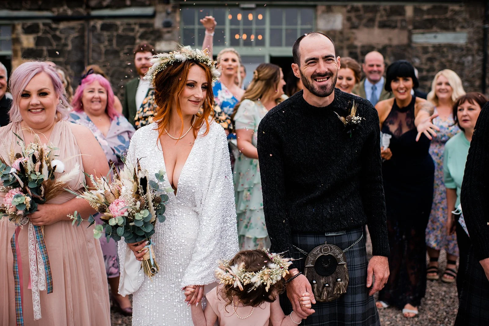 The groom smiles as confetti falls around the couple and their flower girl in the courtyard.