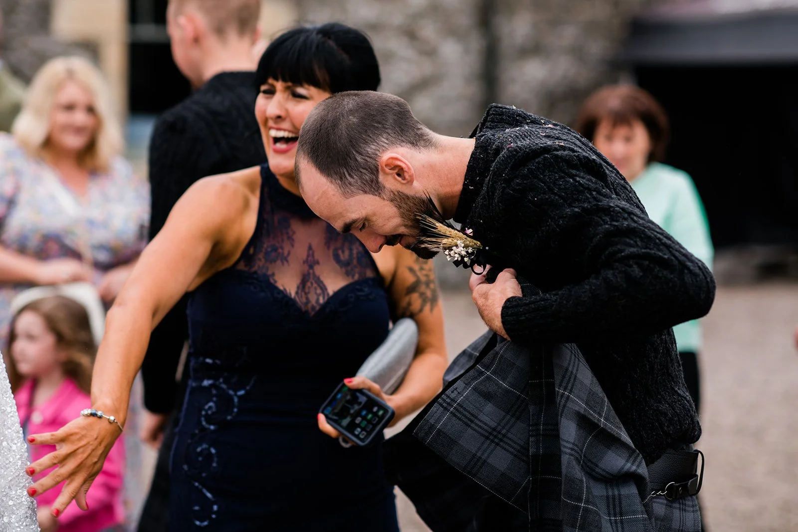 The groom hugs a laughing wedding guest during the drinks reception.