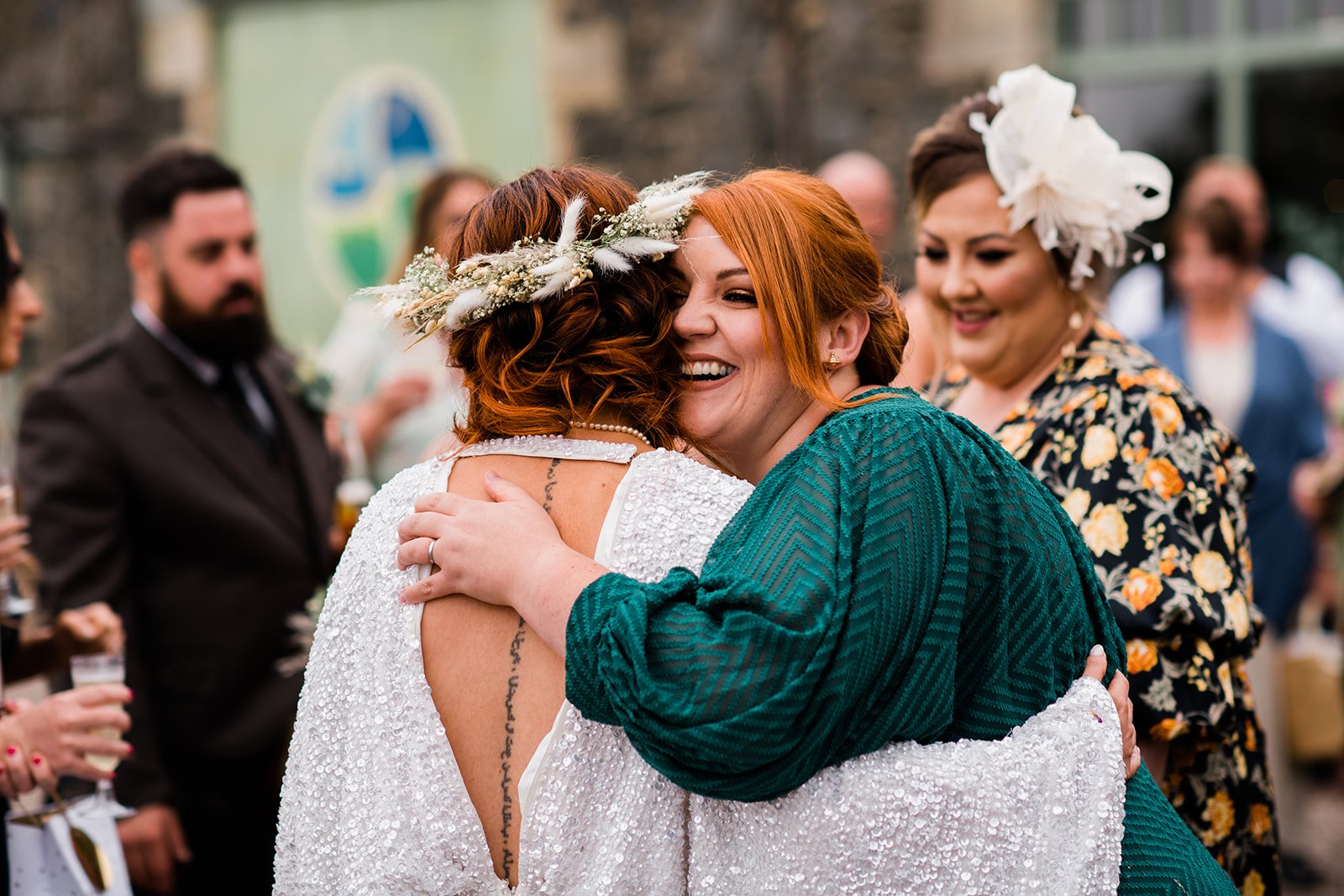 The bride embraces a wedding guest in a green dress outside Pratis Barns.