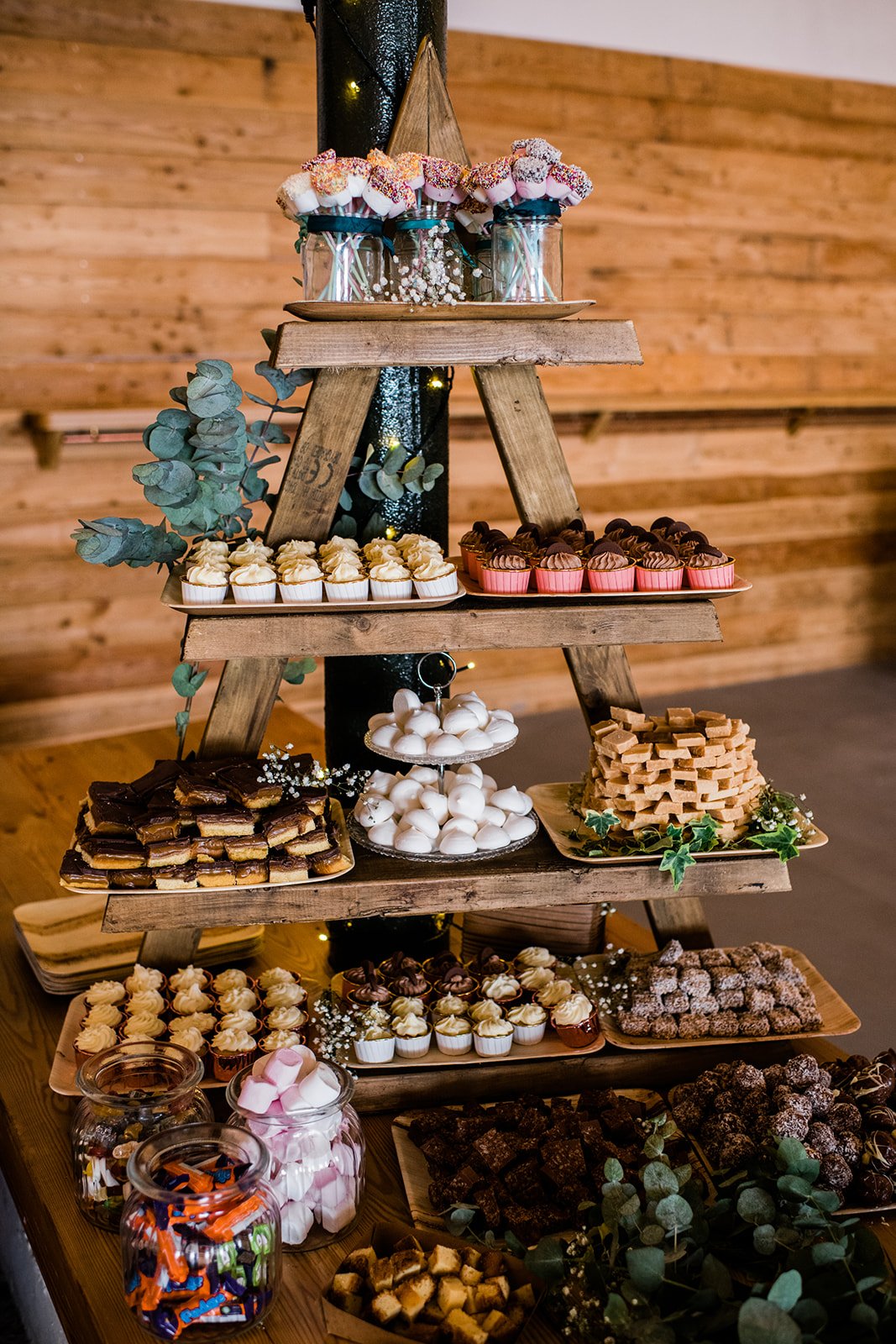 A rustic wooden ladder displays cakes and sweet treats at the wedding reception.