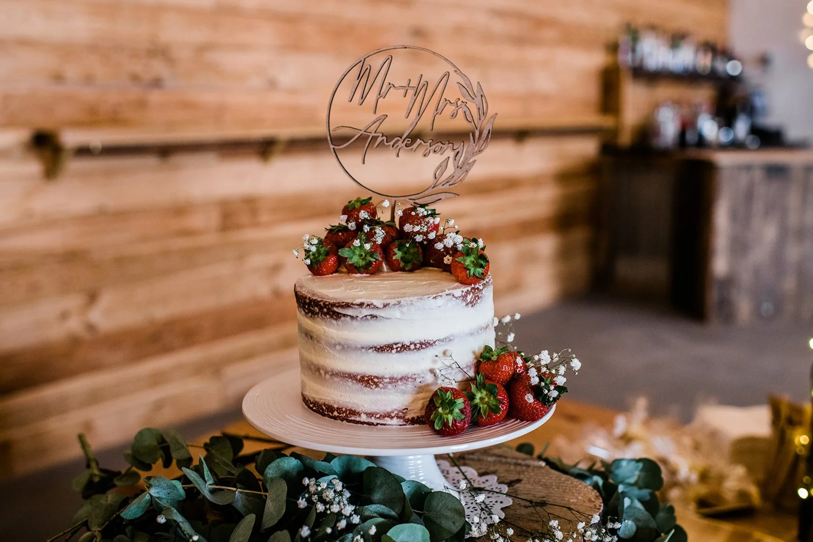 A semi-naked wedding cake decorated with berries and a personalised topper.