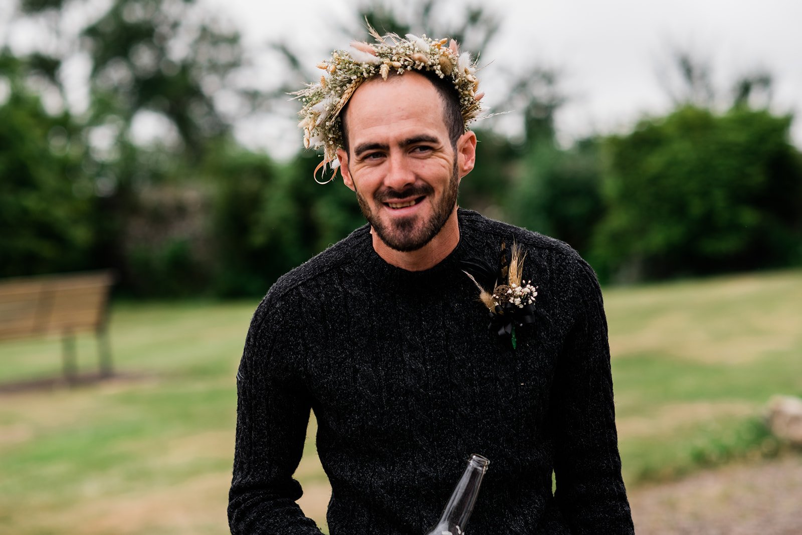 The groom wears the bride’s flower crown and laughs outside Pratis Barns.