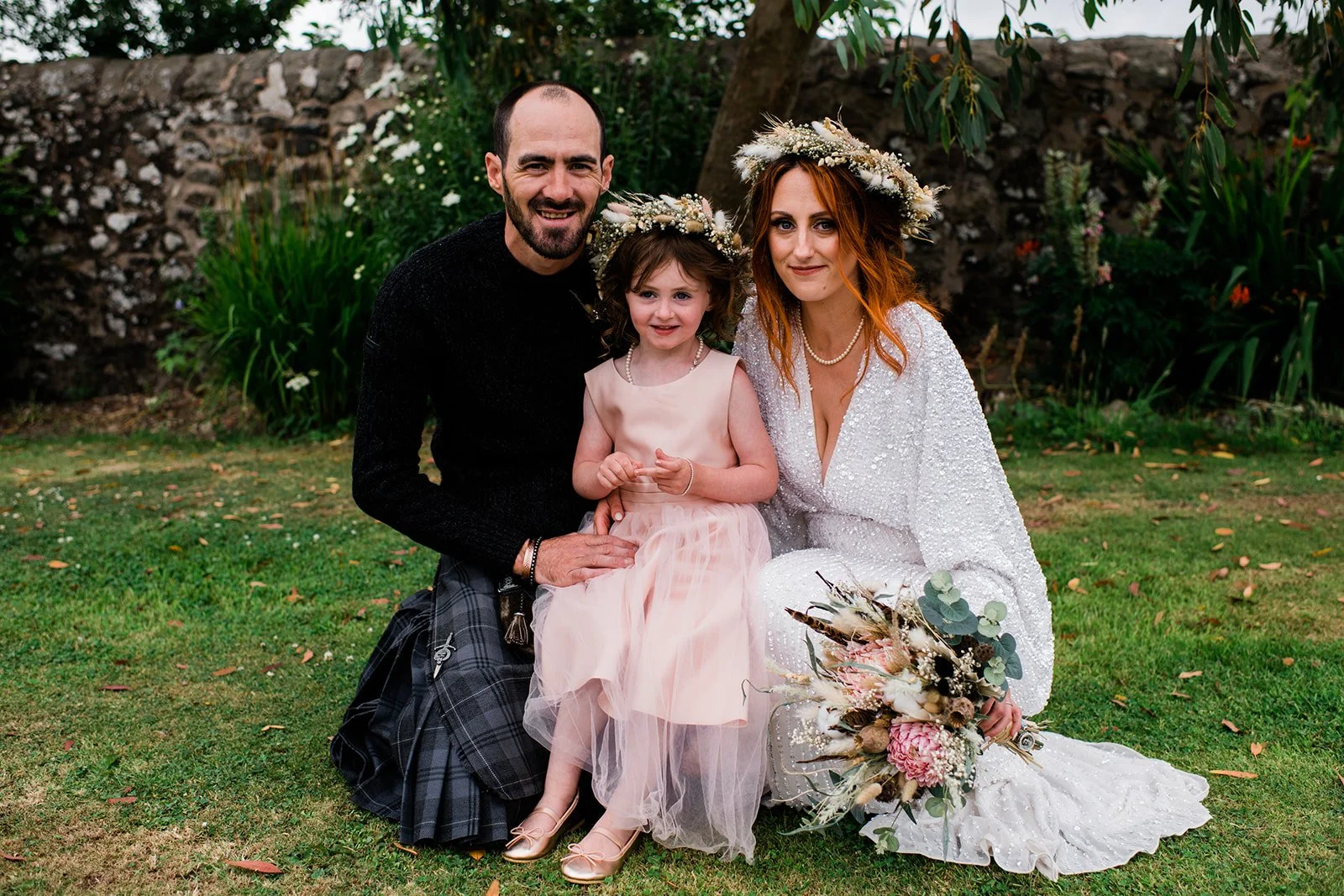 The newly married couple pose with a young flower girl in the gardens at Pratis Barns.