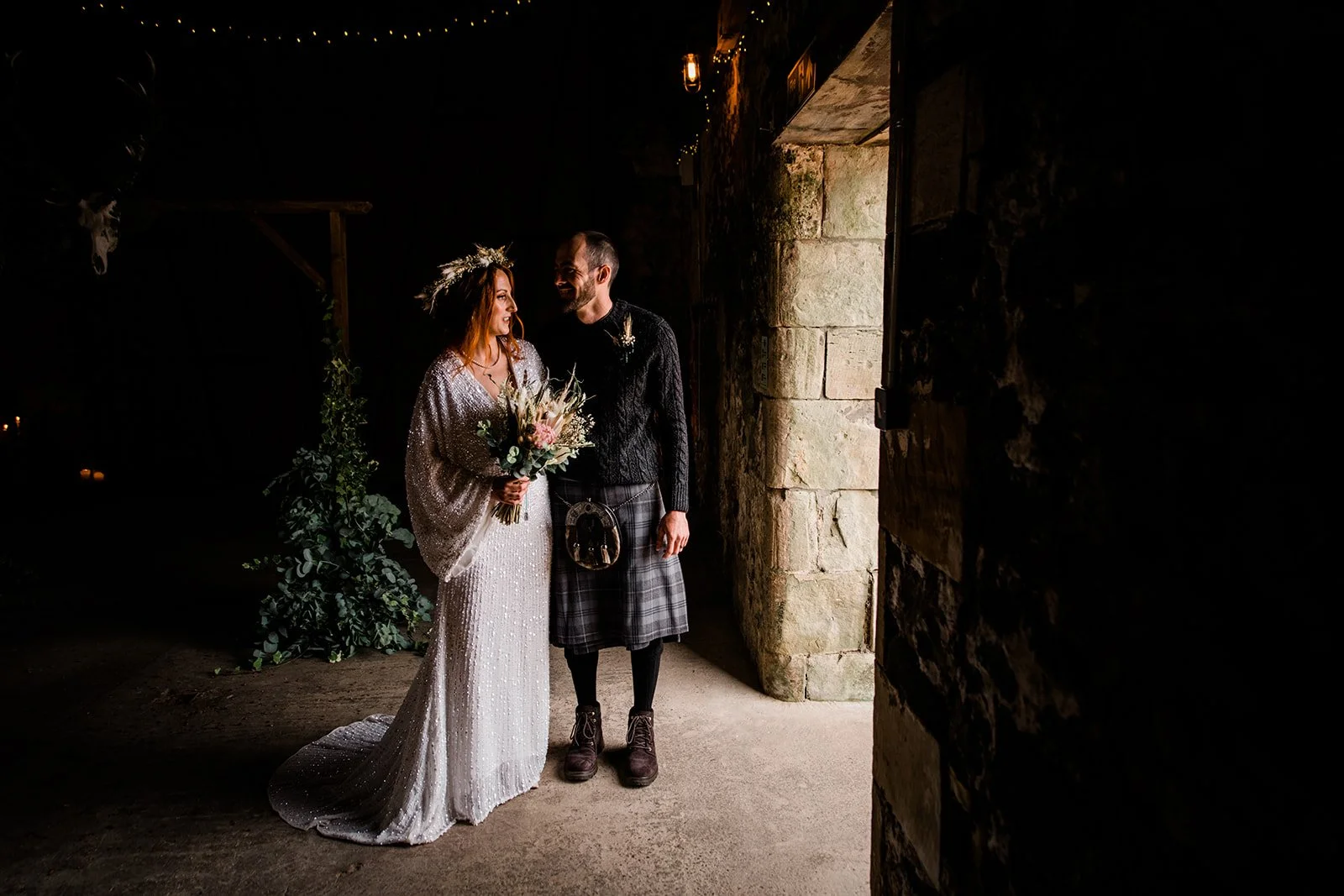 Bride and groom stand together in a shaft of light inside the rustic stone barn.