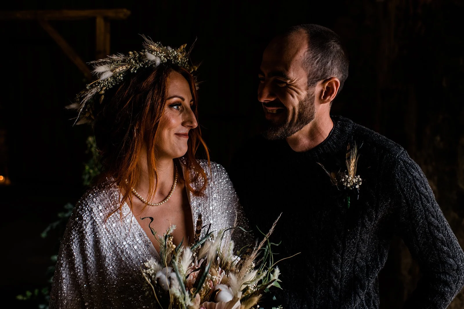 The couple smile at each other during a softly lit portrait inside Pratis Barns.