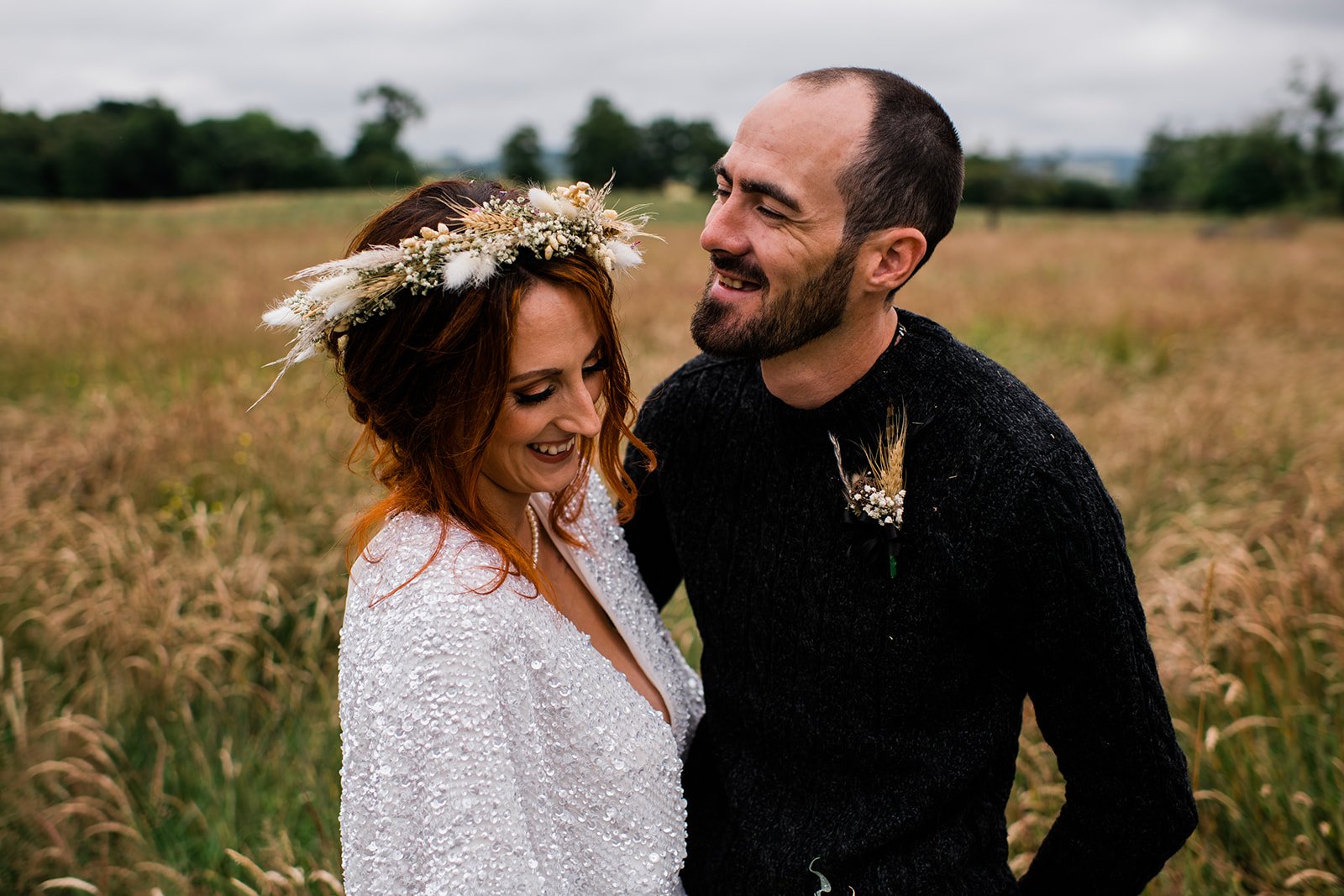 The couple laugh together during their wedding portraits in a meadow.