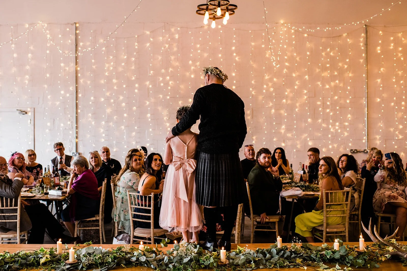 Guests watch the groom and a young flower girl at the front of the reception room.