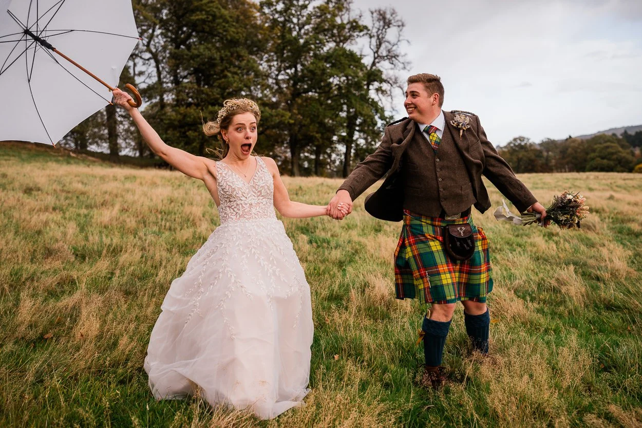 fun-picture-of-bride-and-Groom-running-down-a-hill-with-an-umbrella-in-the-wind
