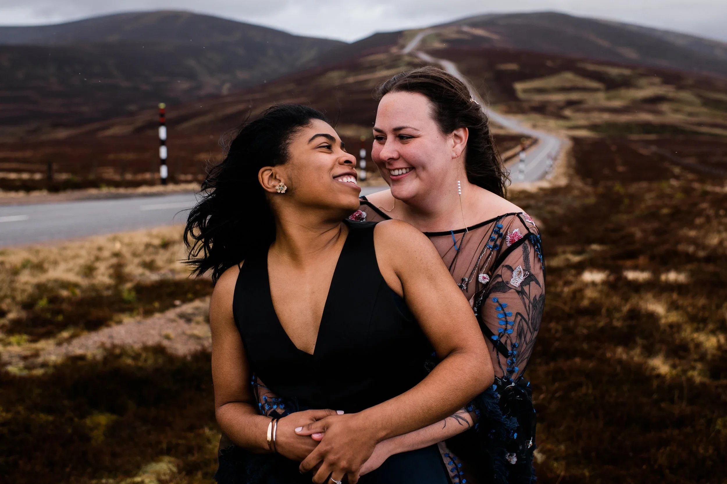 Two brides embracing on a hill during Cairngorms elopement