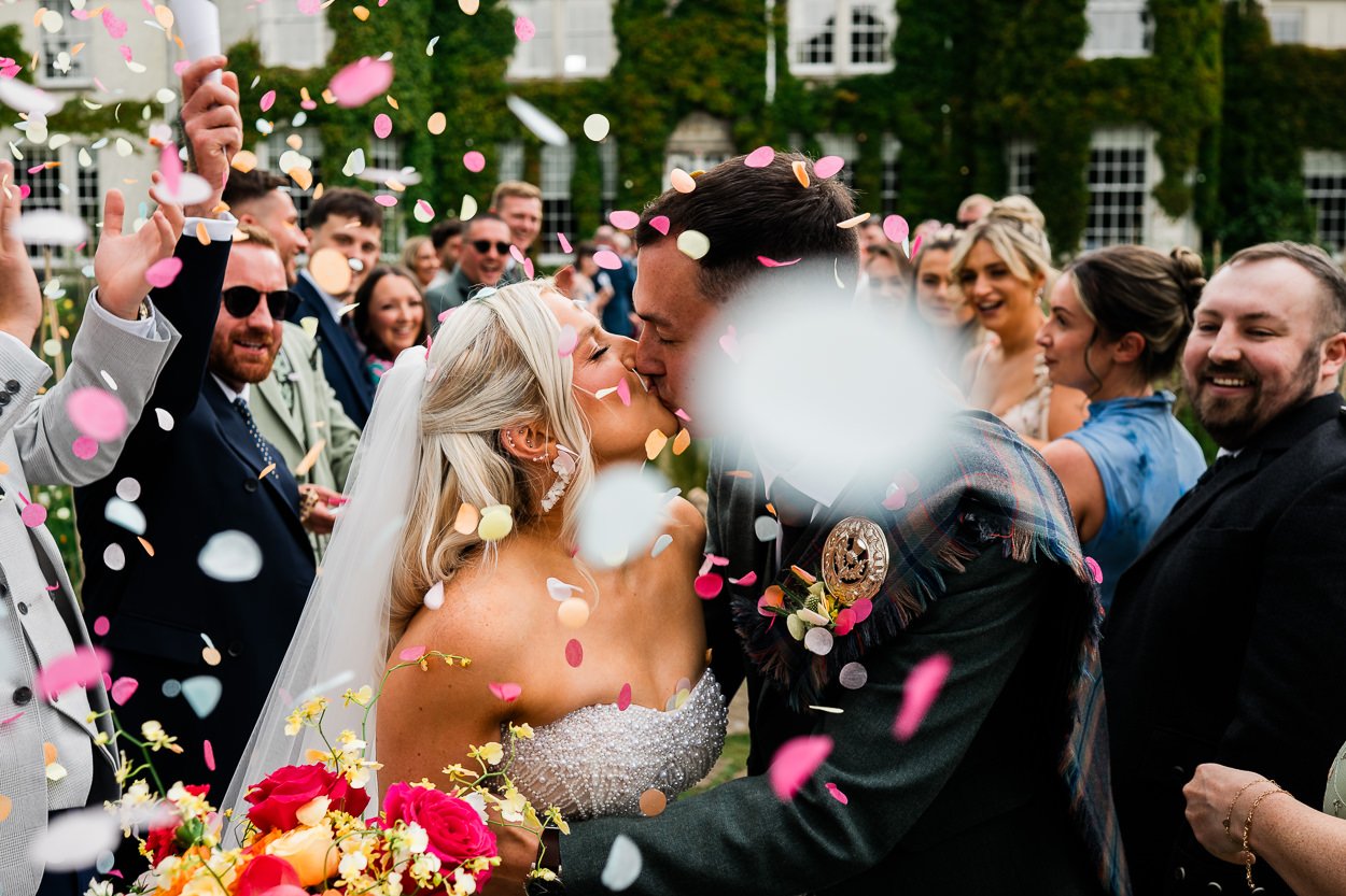 Bride-and-groom-kissing-whilst-being-covered-in-confetti