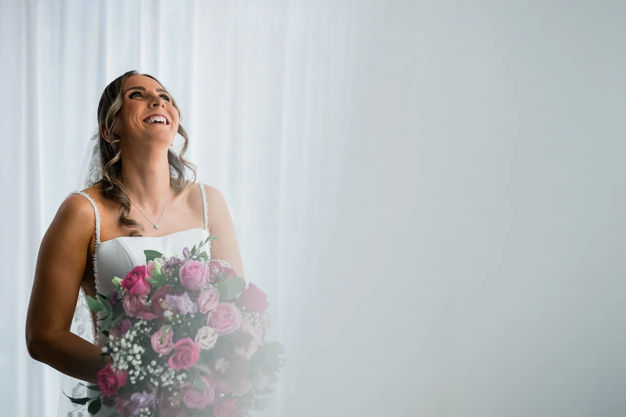 Bride laughing whilst standing next to a window in Glasgow