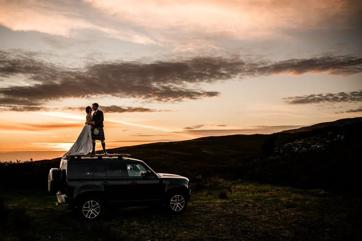 Bride and groom standing on top of their car during sunset on a hill at GG's Yard wedding
