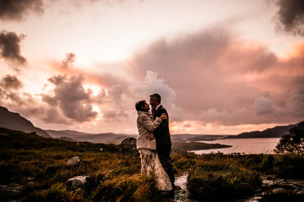 Bride and groom standing in front of dramatic sunset in Torridon during an elopement. 