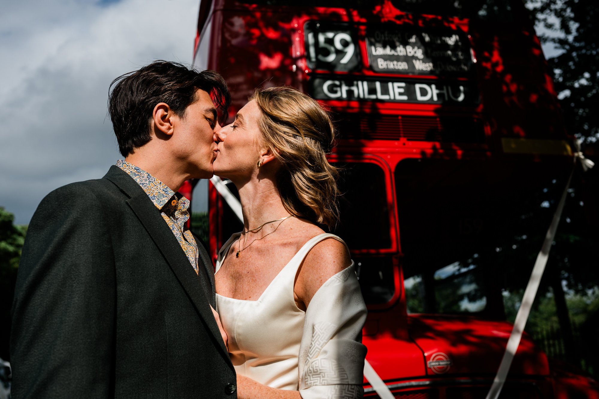 Bride and groom kissing in front of vintage red bus