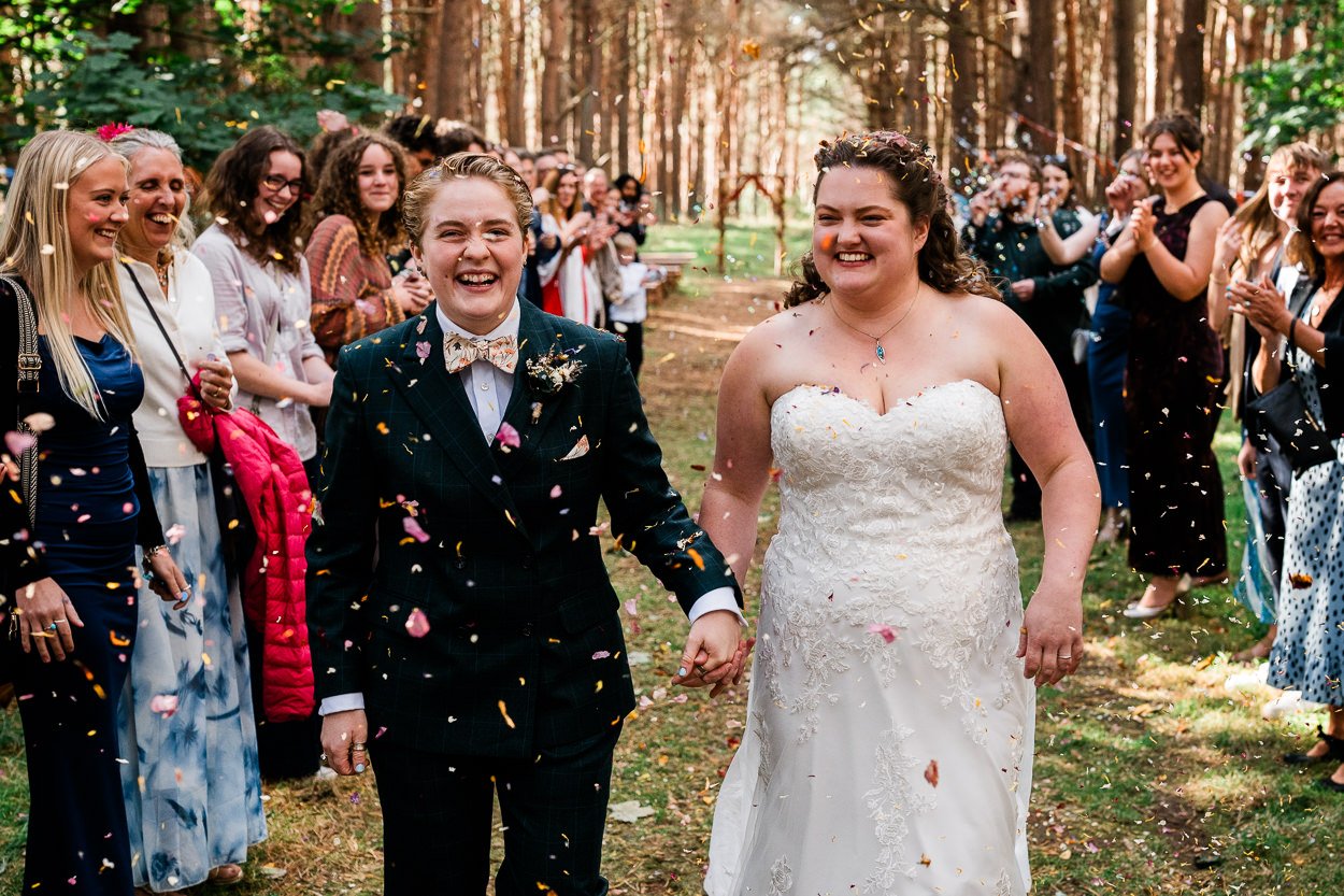 Two brides running through confetti in woodland at Harvest Moon weddings