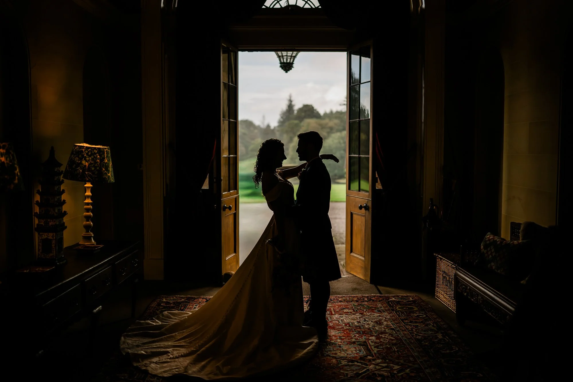 Aimee and Matthew silhouetted in the open doorway of Kinmount House, with the bride’s train across the floor.