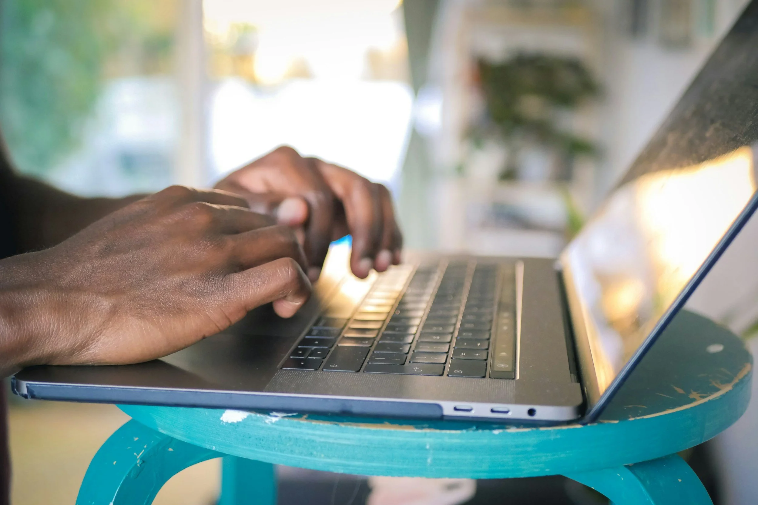 Black hands hover over a laptop keyboard
