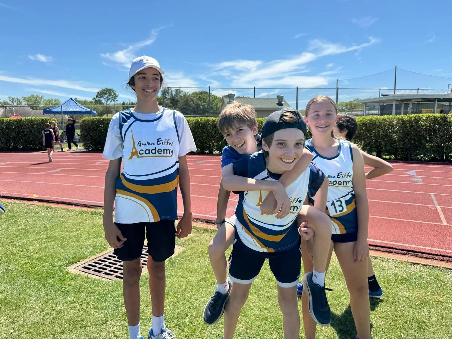 Group of young athletes in track and field uniforms smiling outdoors on a sunny day.