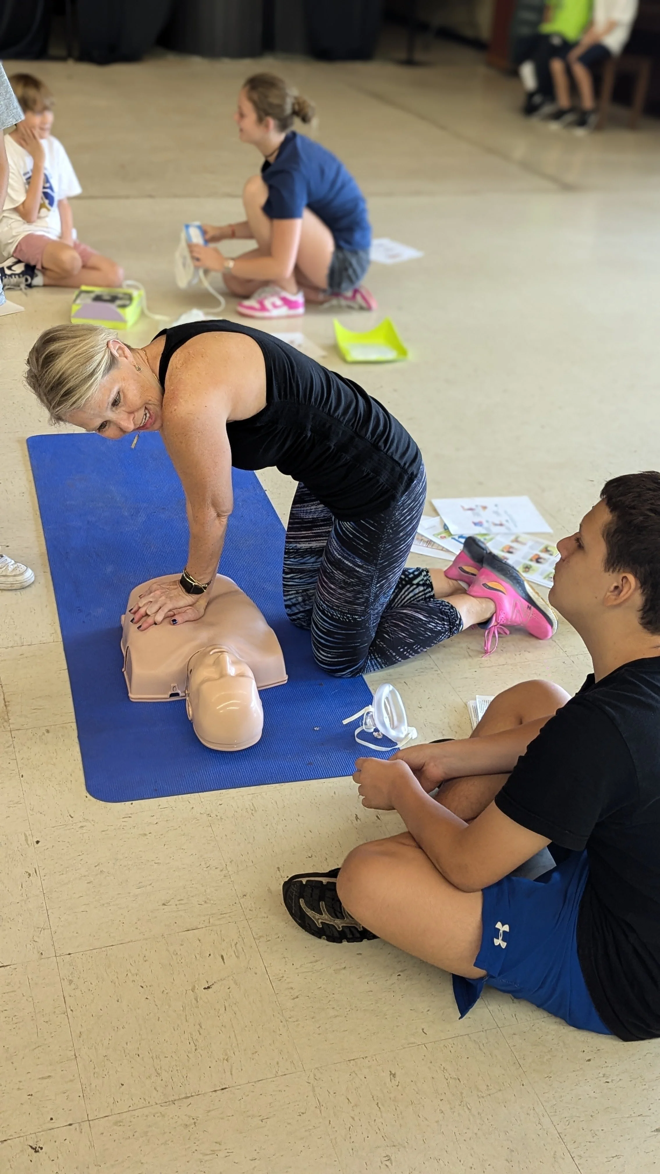 A woman practicing CPR on a training manikin while others observe in a classroom setting.