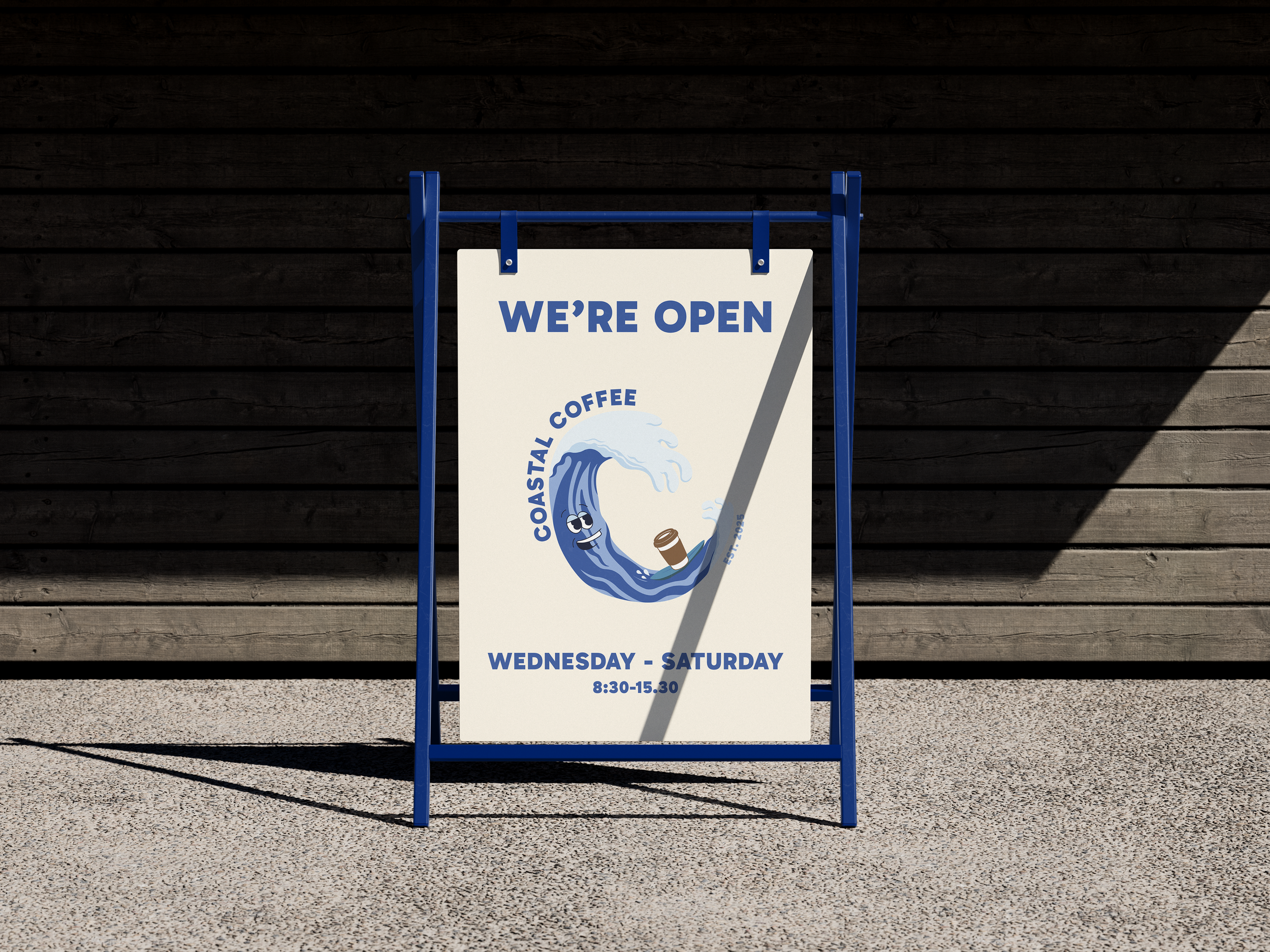 A sidewalk sign outdoors on a textured surface in front of a dark wooden wall, advertising a coffee shop called Coastal Coffee. The sign features a cartoon wave with a face holding a coffee cup, with text indicating the shop is open Wednesday to Saturday from 8:30 to 15:30.