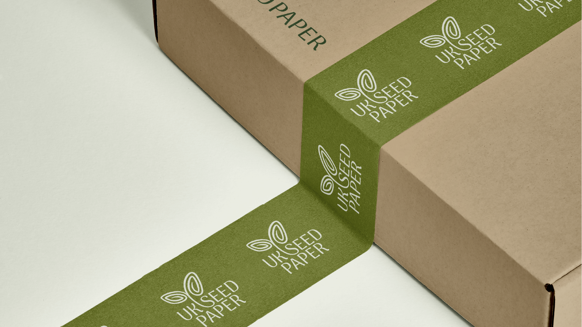 Close-up of a cardboard box sealed with green tape labeled 'UK Seed Paper' and featuring a seedling logo.