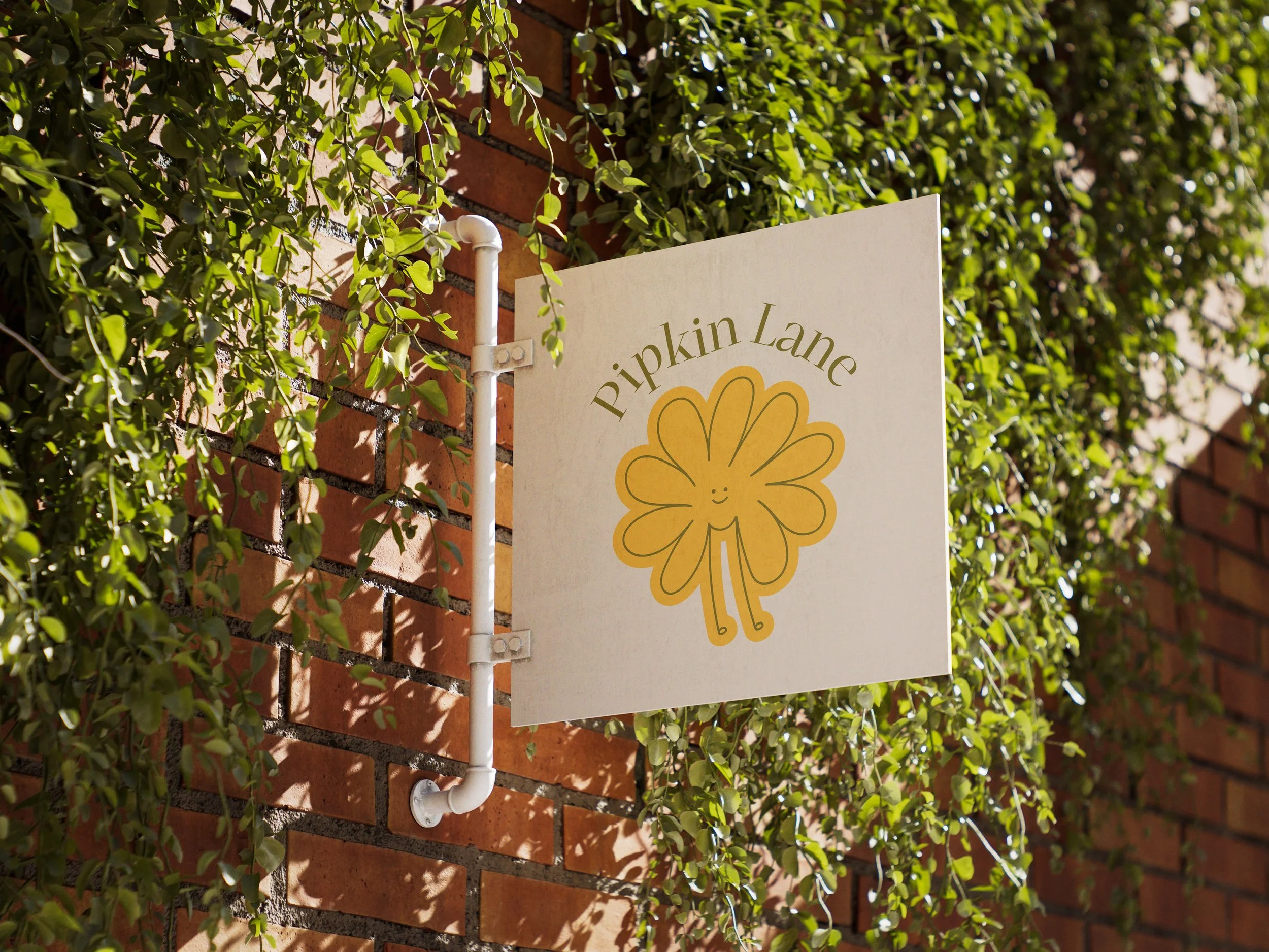 A white sign with yellow and green writing that reads 'Pipkin Lane' and a cute, smiling, yellow flower character, attached to a brick wall with greenery around it.