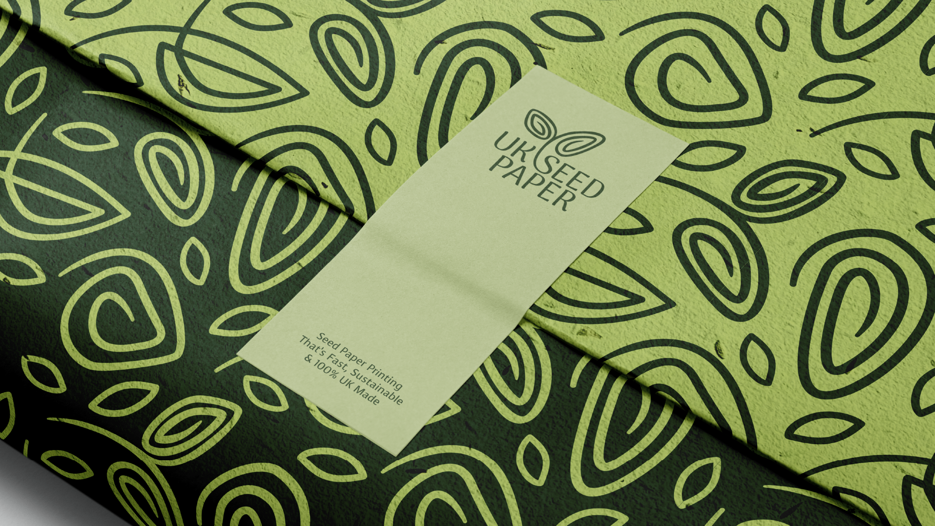 Close-up of UK Seed Paper, featuring a green patterned design with black seed shapes and a label indicating it is eco-friendly seed paper printing, sustainable, UK made.