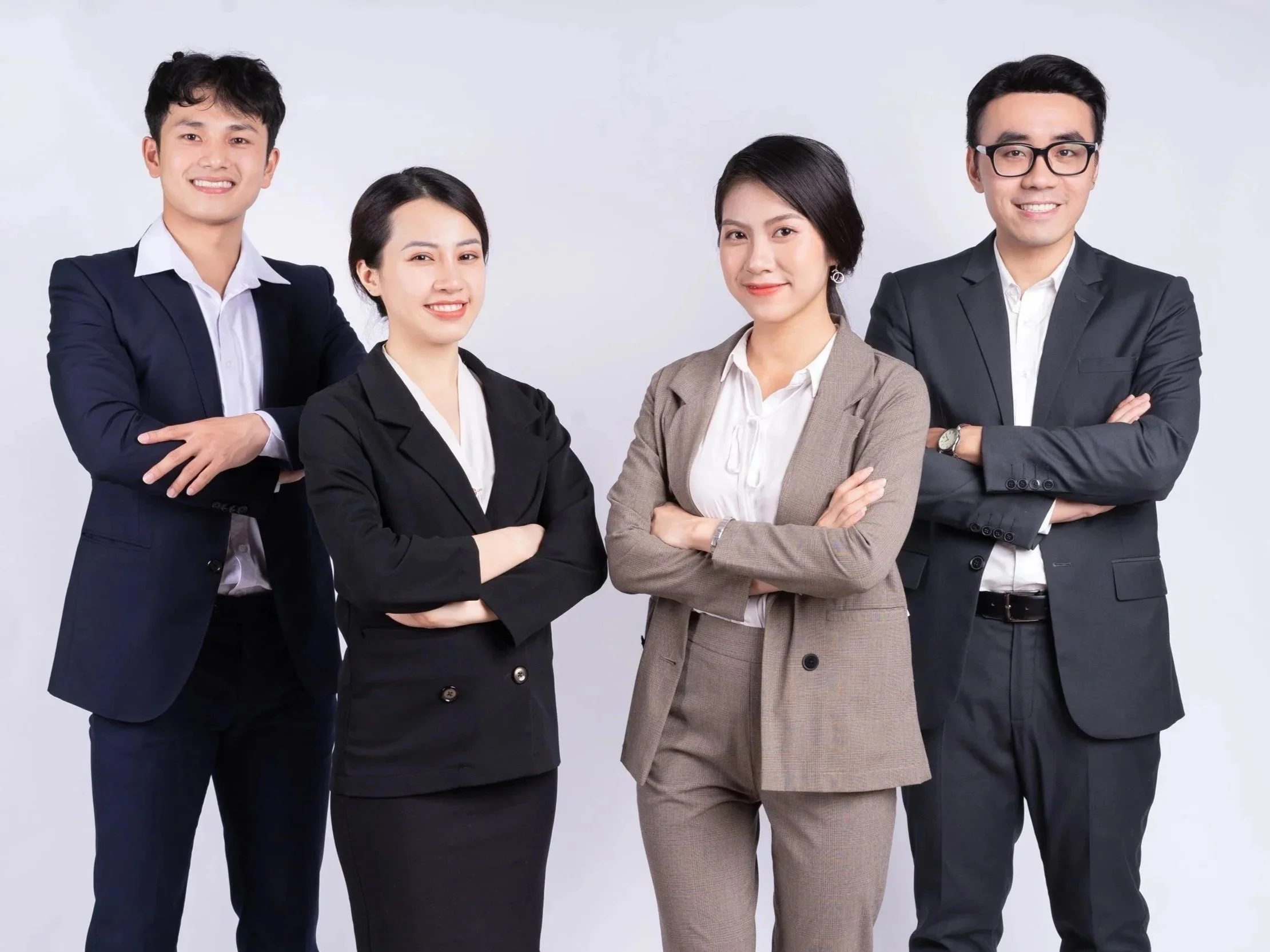 Four diverse business professionals standing confidently with arms crossed against a plain background.