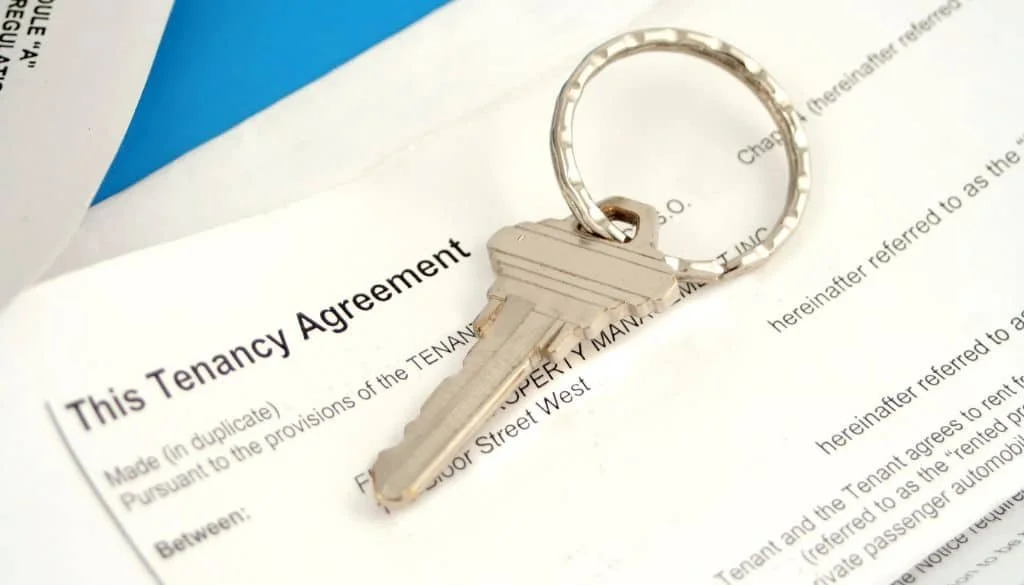 A close-up view of a silver house key on top of a sample tenancy agreement (lease)