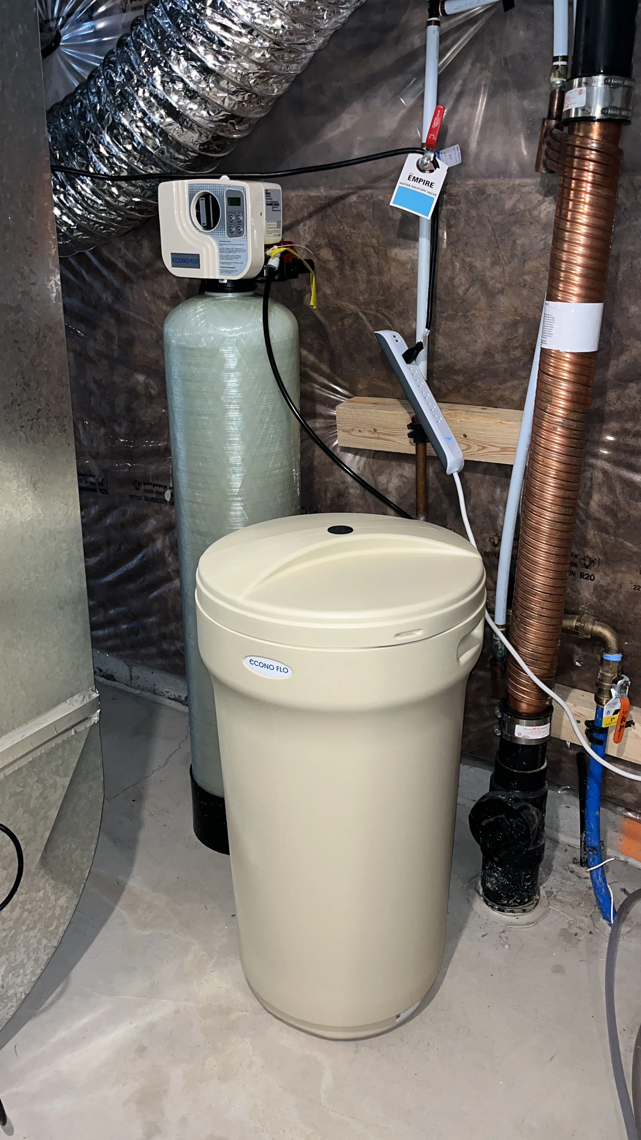 Installation of a water softener and filtration system in a utility room, featuring pipes, hoses, and a control valve.