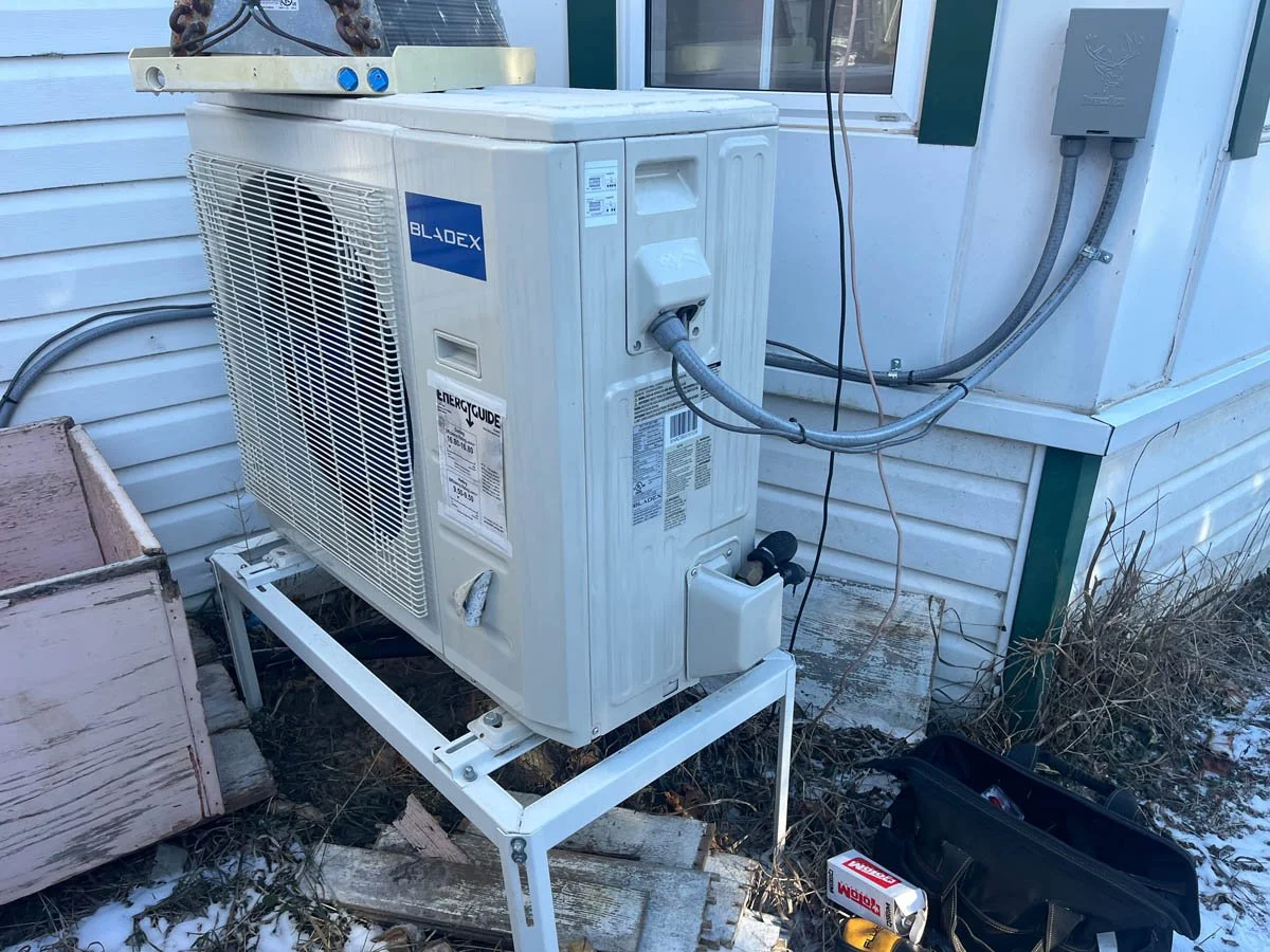 Outdoor HVAC unit with wires and tools nearby outside a house.