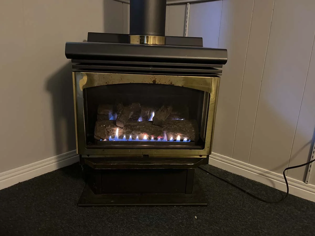 Gas fireplace with visible flames and ceramic logs inside a living room corner.