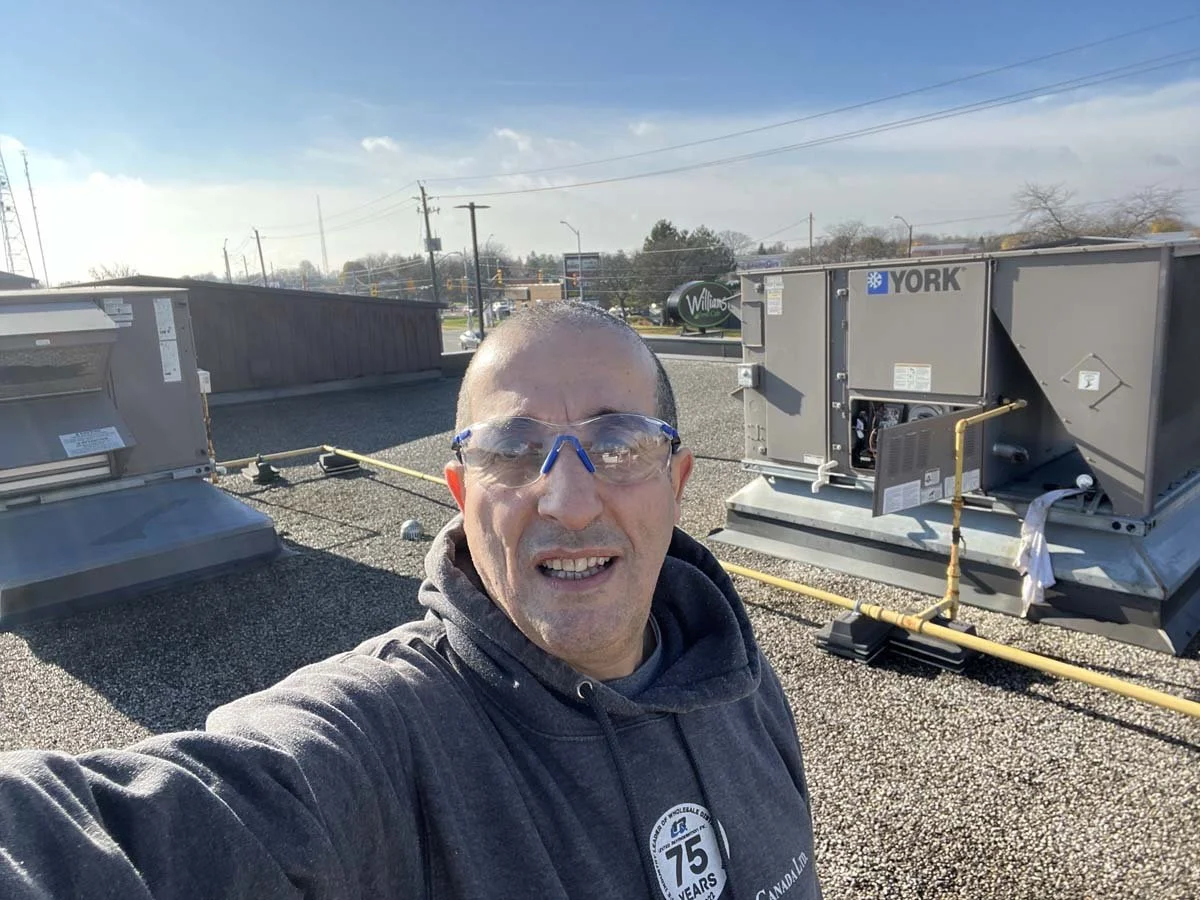 Man wearing safety goggles and a hoodie taking a selfie on a rooftop with HVAC units and a clear sky.
