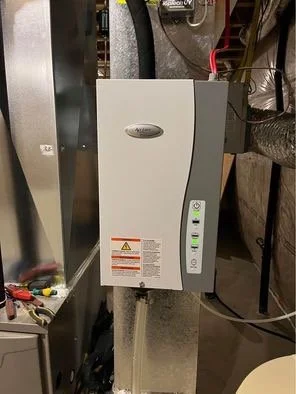 A gray and black tankless water heater mounted on a wall in a utility room.