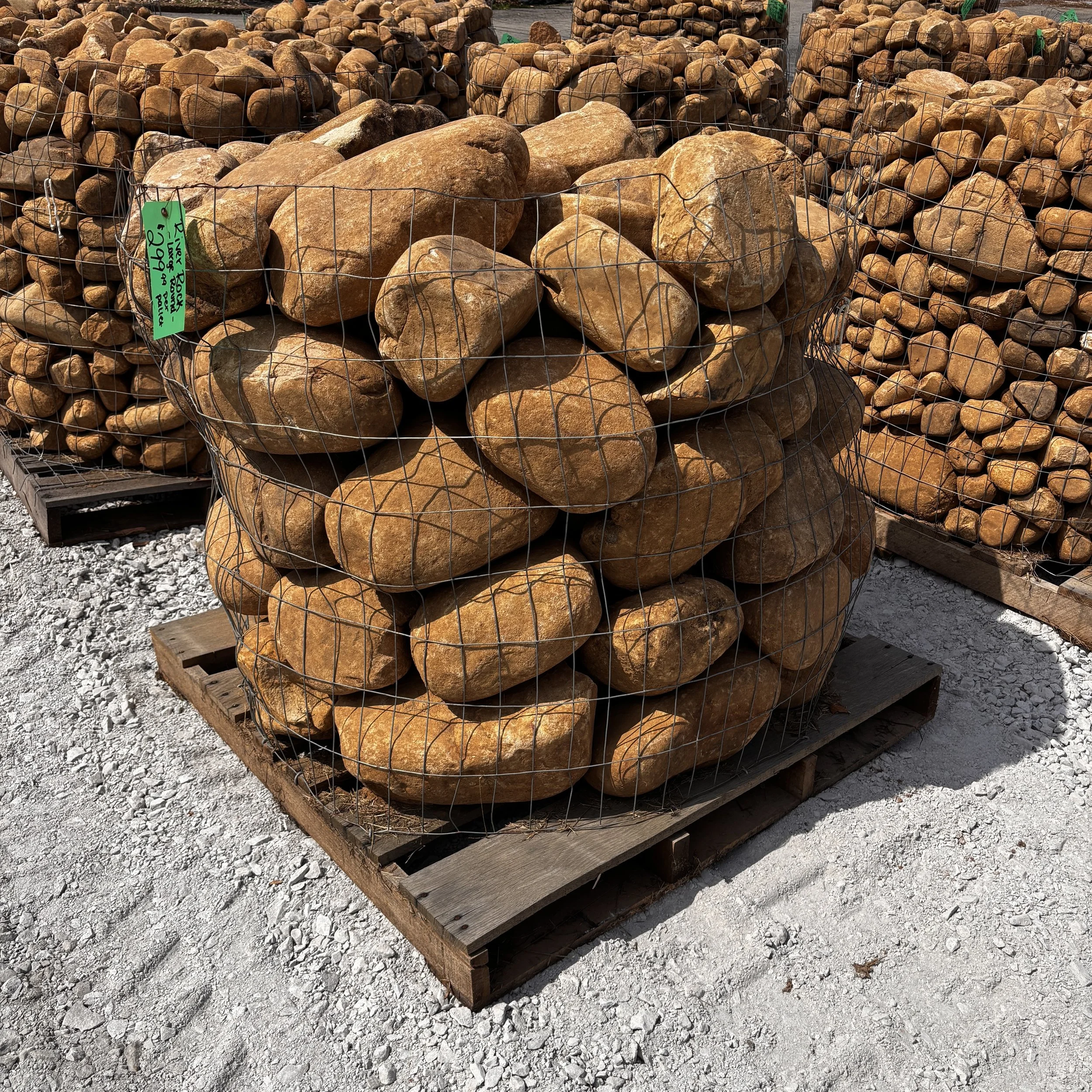 Large rocks stored inside metal wire cages on wooden pallets at a gravel yard.