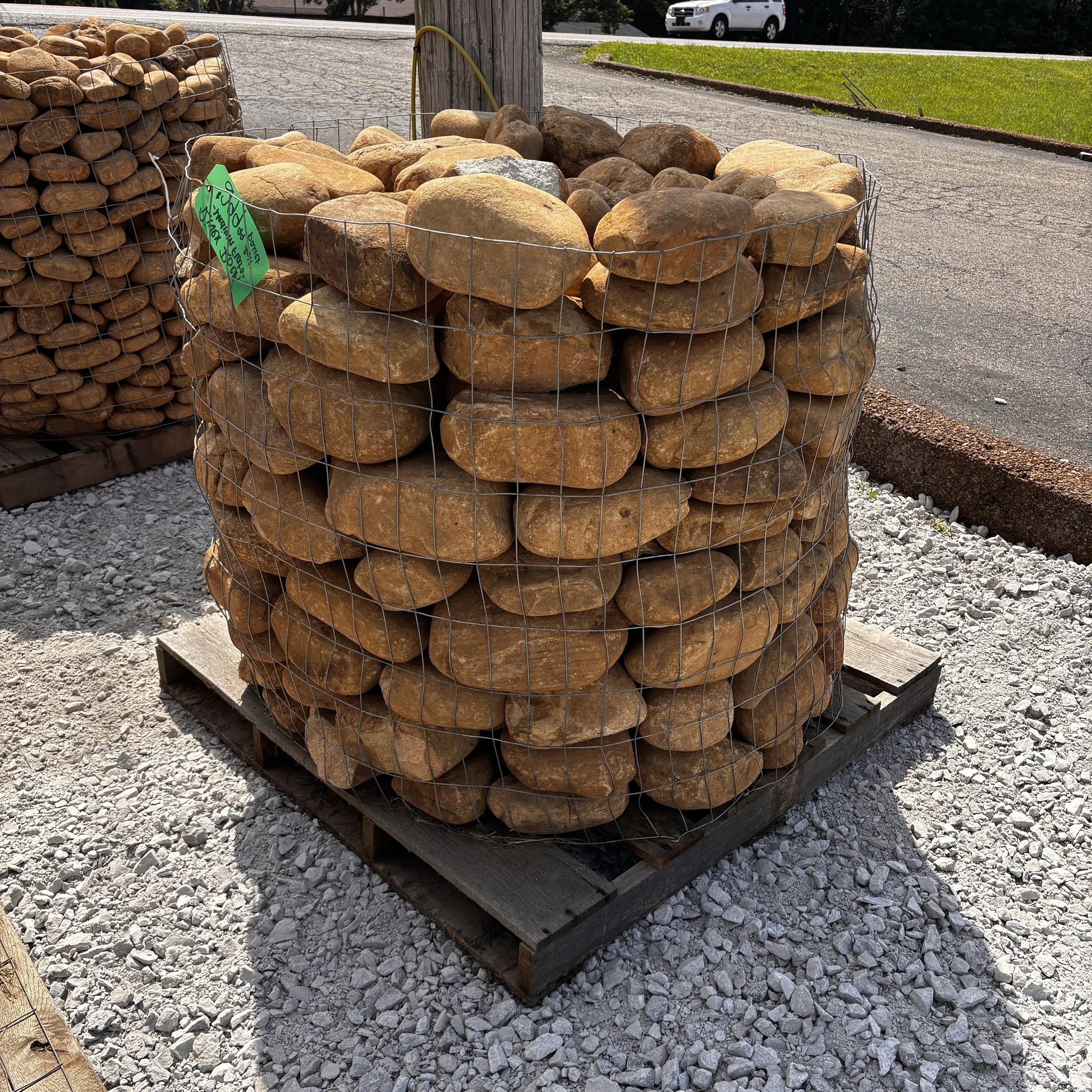 Piles of large stones or rocks placed in wire cages on pallets for sale or construction, with a green price tag attached.