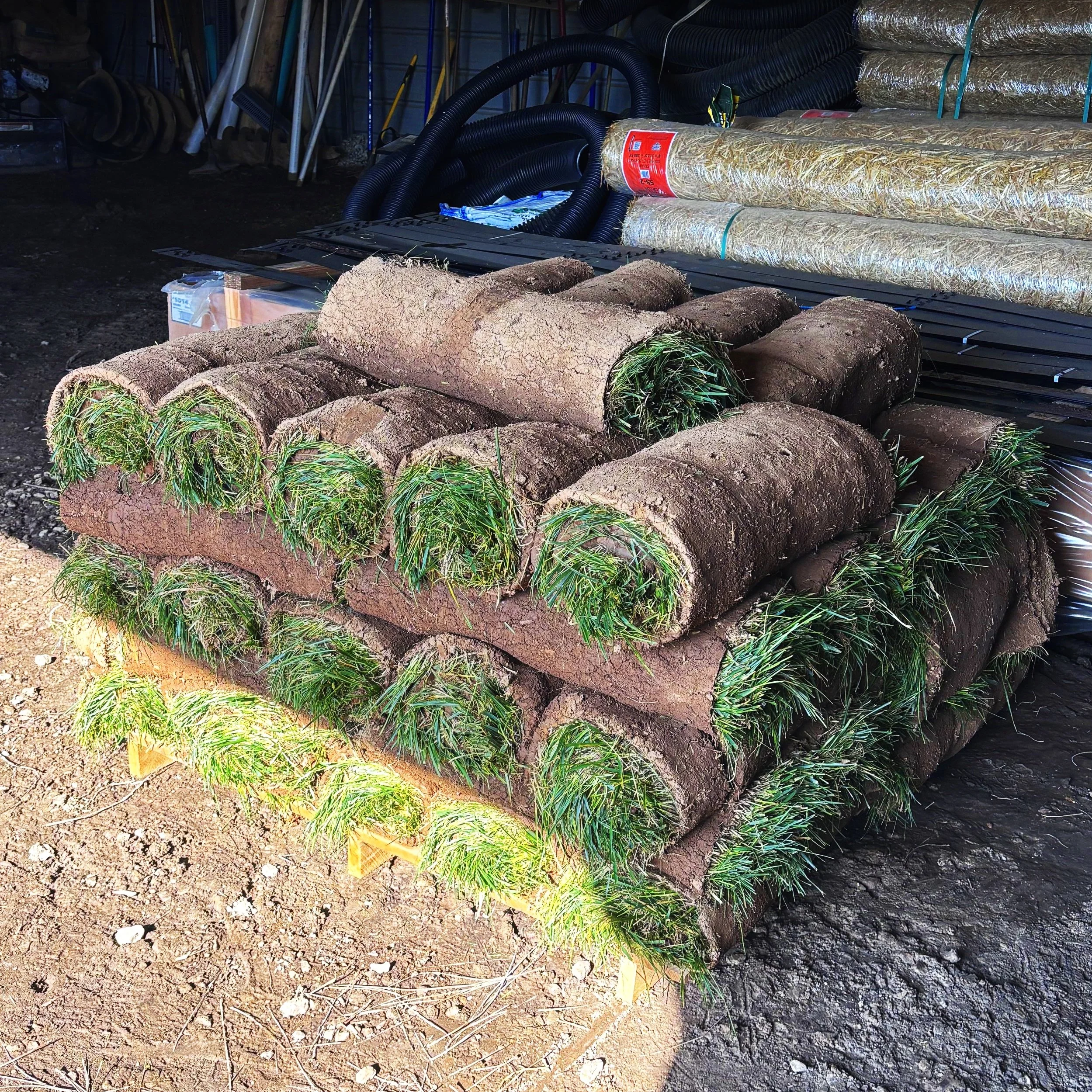 Piles of rolled sod grass stacked in a storage area with tools and insulation materials in the background.