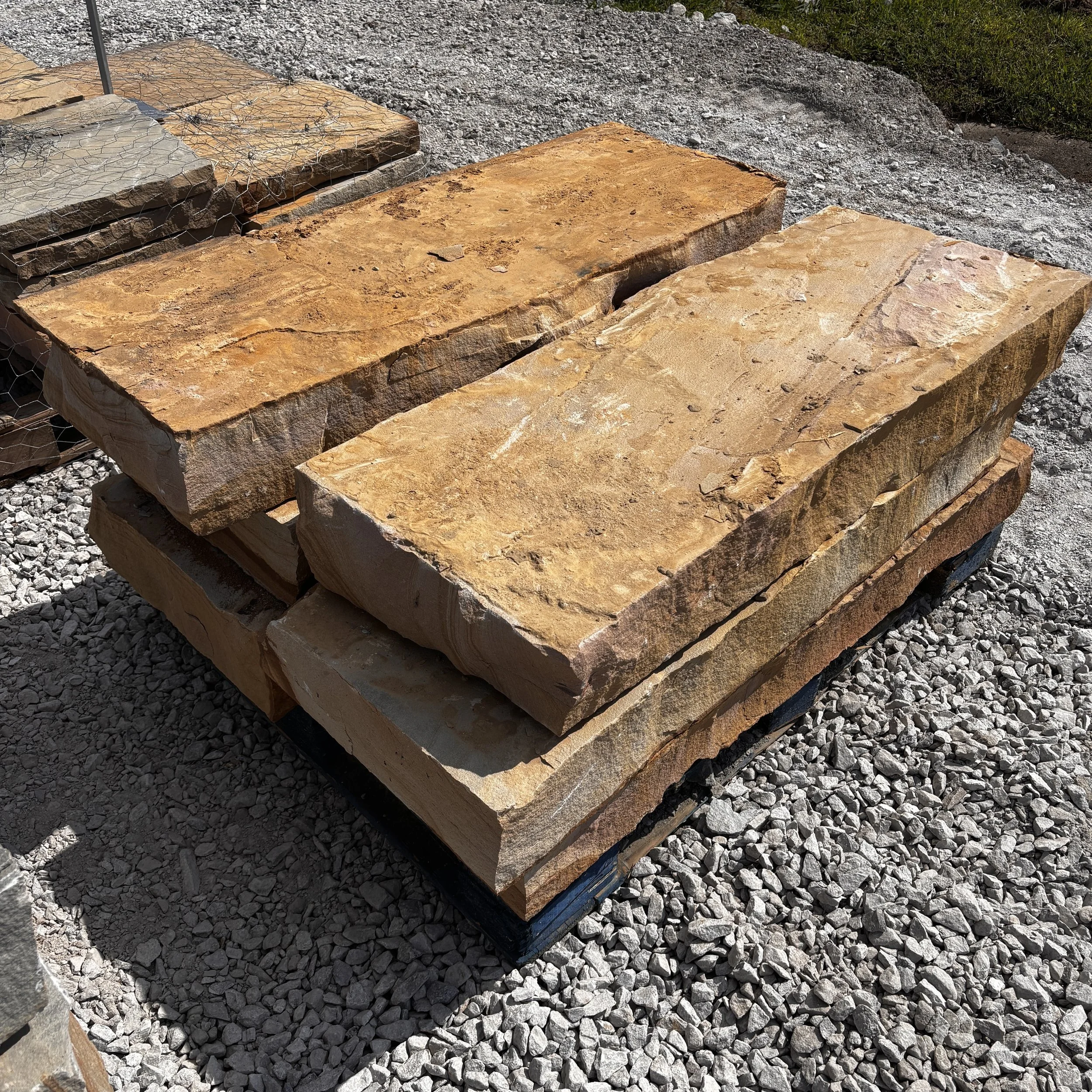 Stacked sandstone blocks outdoors on gravel ground with gravel and grass in background.