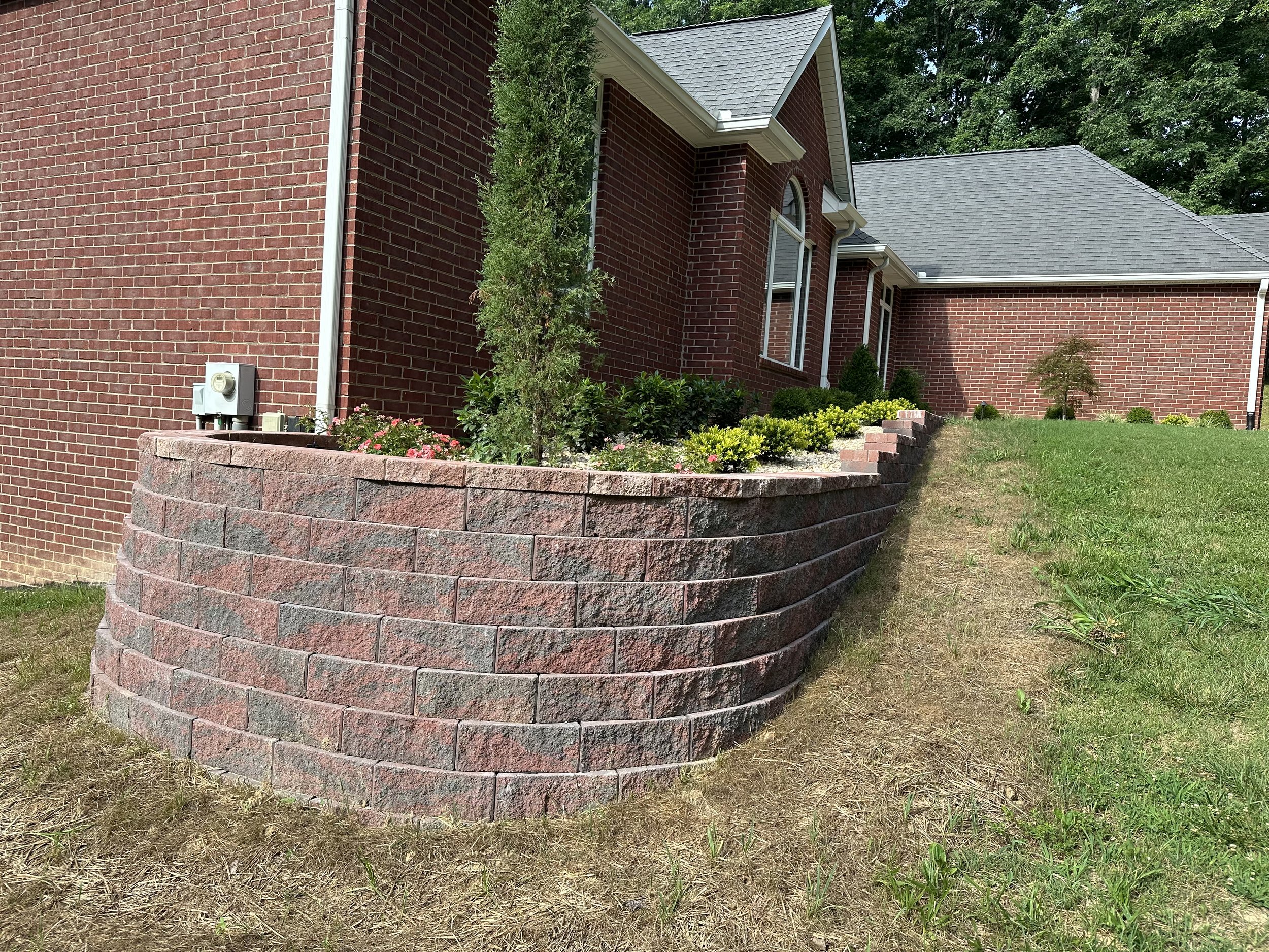 Red brick house with a curved brick retaining wall, small trees, and a flower bed in front.
